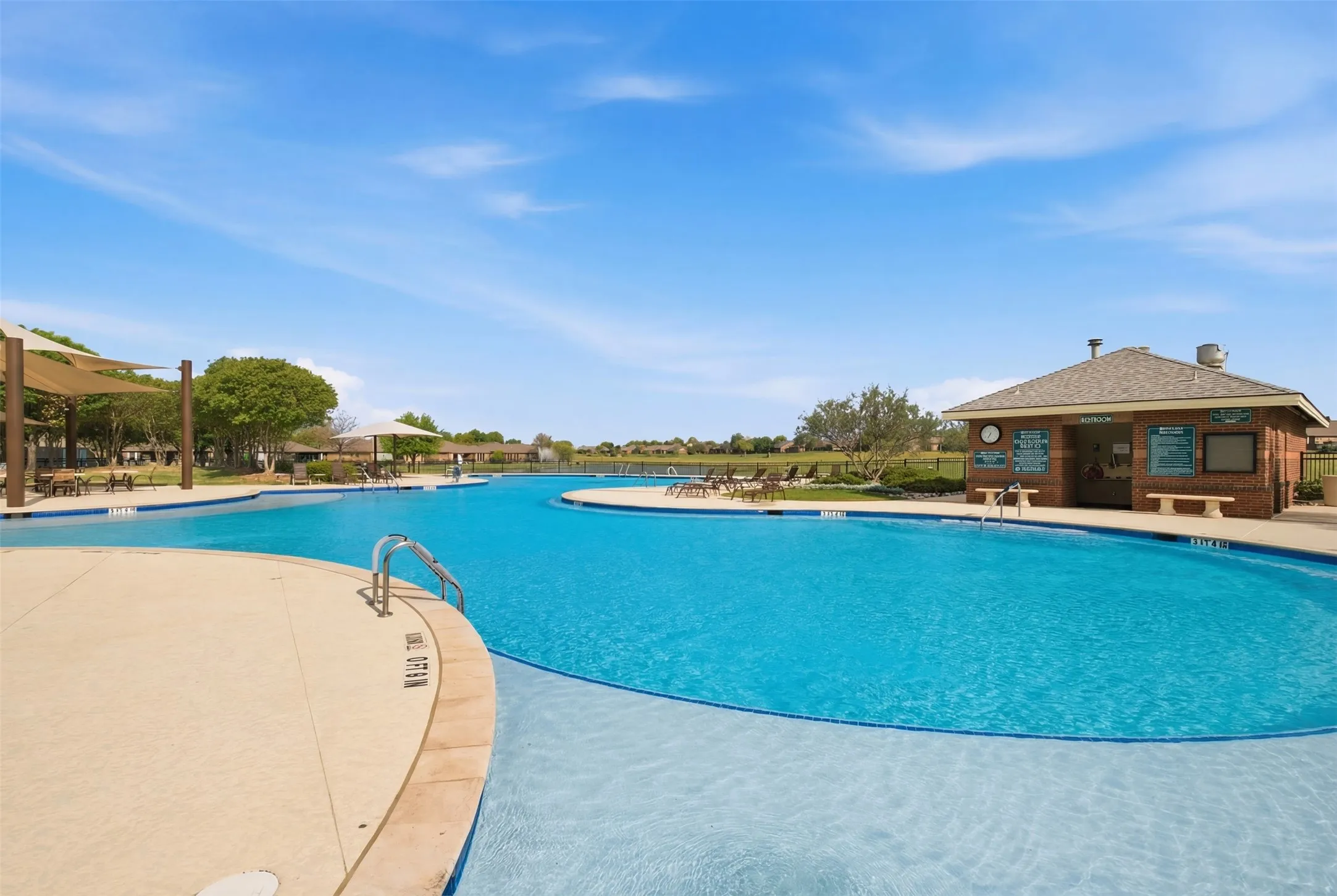 Expansive community pool with integrated shallow entry, a poolside building with a pitched roof, and multiple shaded lounge areas