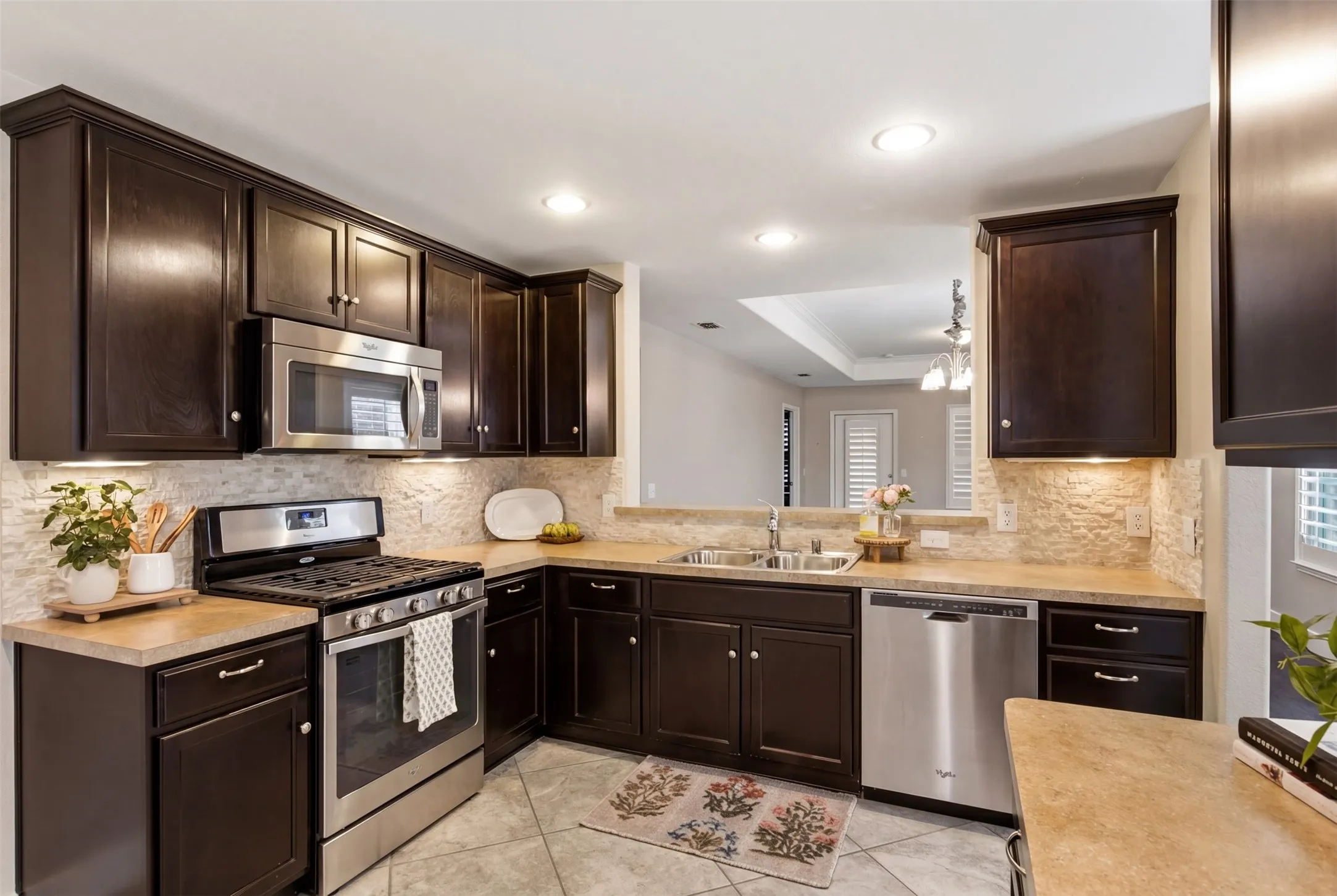 Kitchen featuring dark wood-finish cabinetry, stainless steel appliances, stone-look countertops, and a tile backsplash