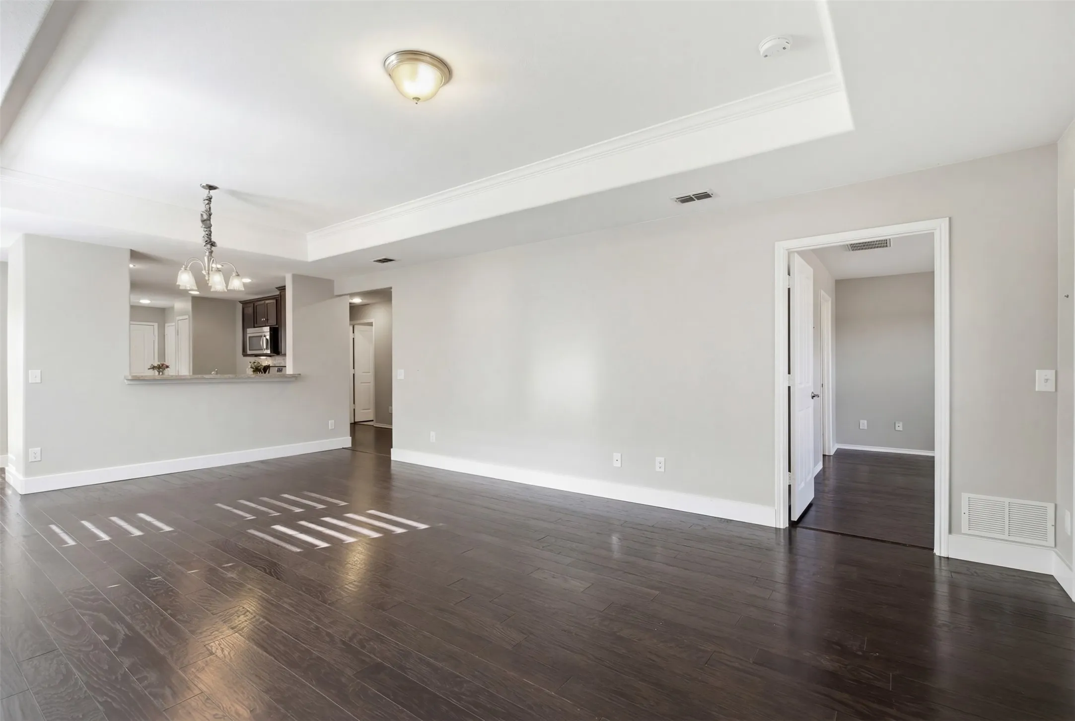 Dark wood-finish flooring, light grey wall paint, tray ceiling, recessed lighting, and a breakfast bar