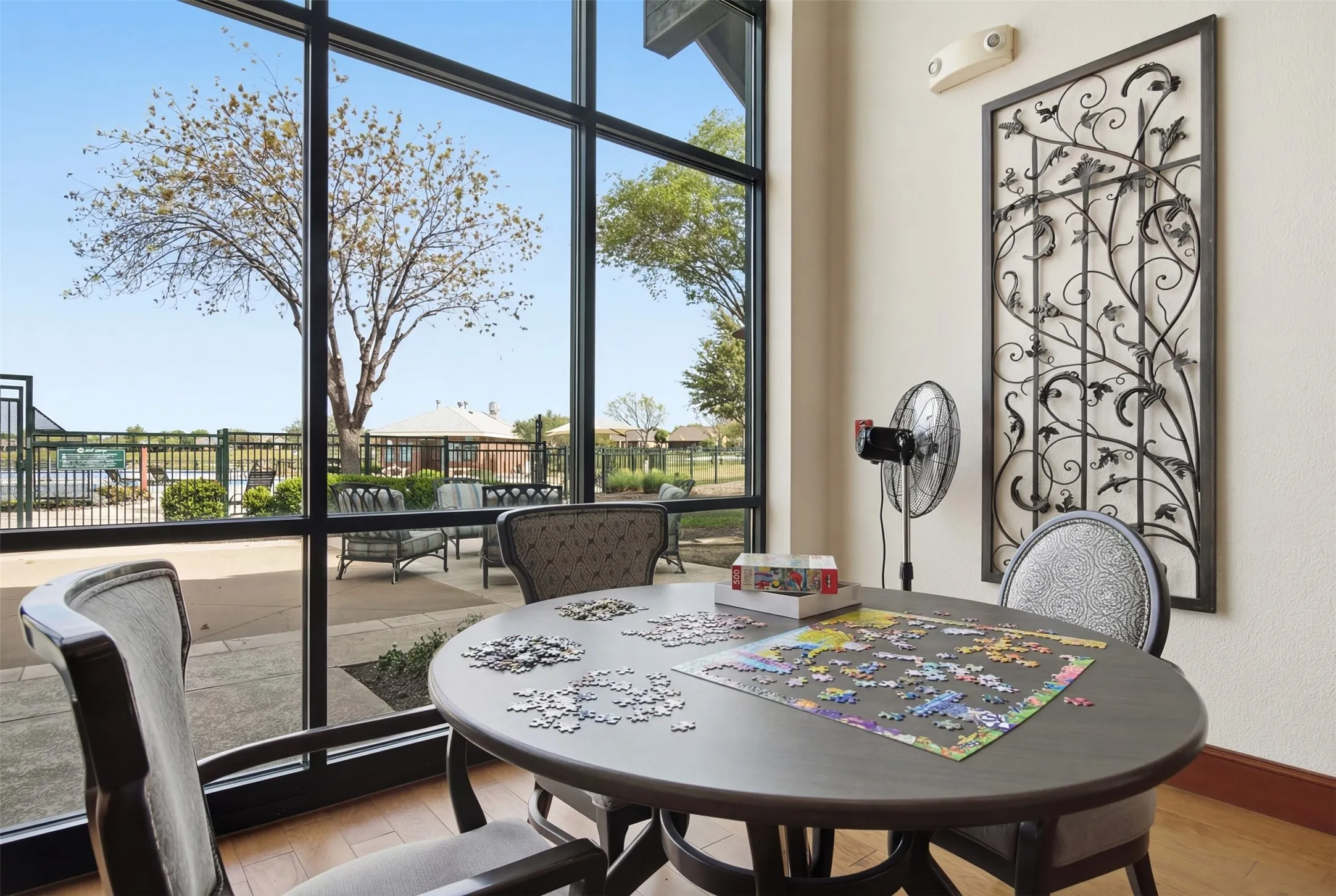 Full-height window paneling, ornamental metal wall art, light-toned textured wall, wood-finish flooring, and upholstered chairs