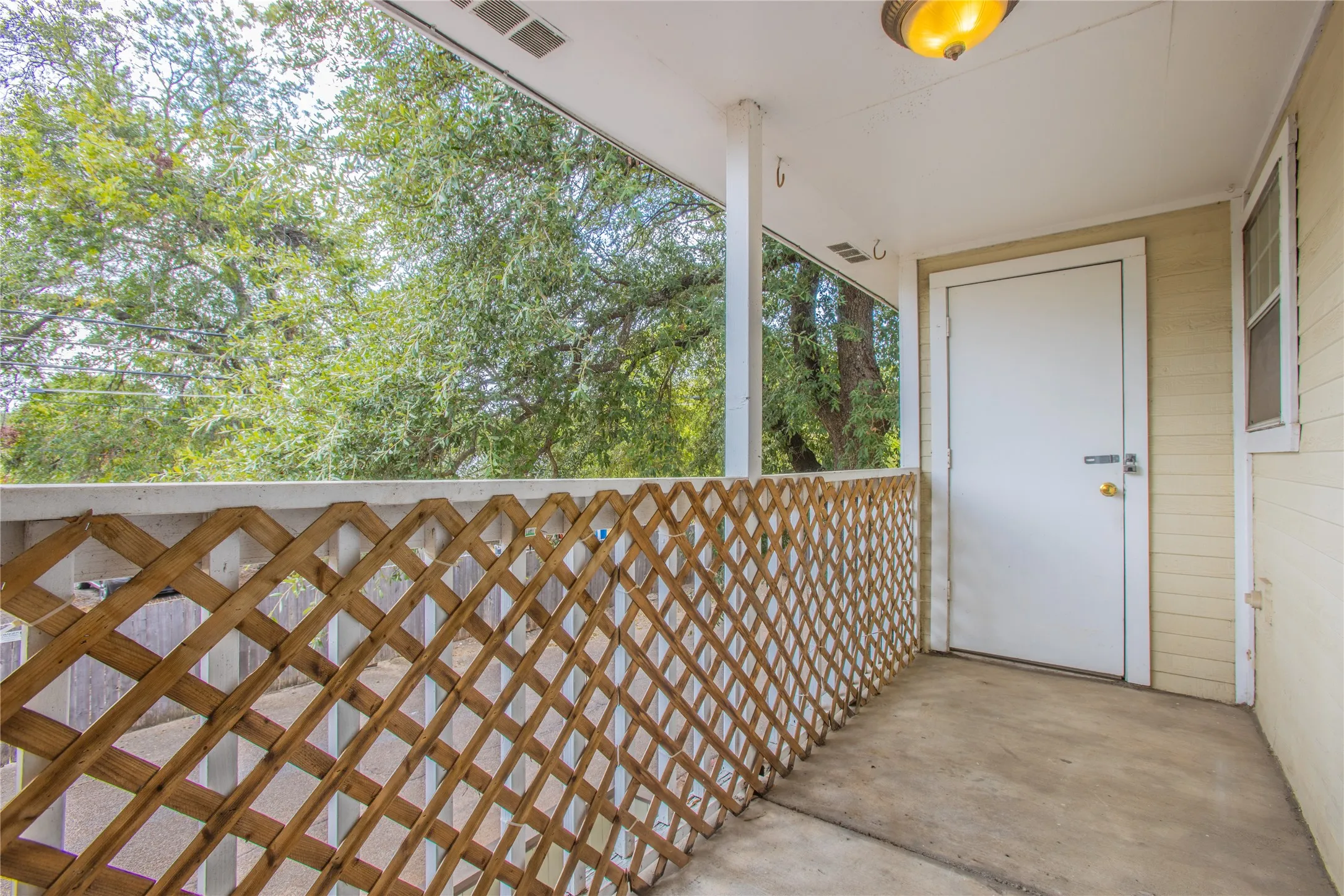 Covered porch with concrete flooring, wood lattice railing, white support columns, and an overhead light fixture