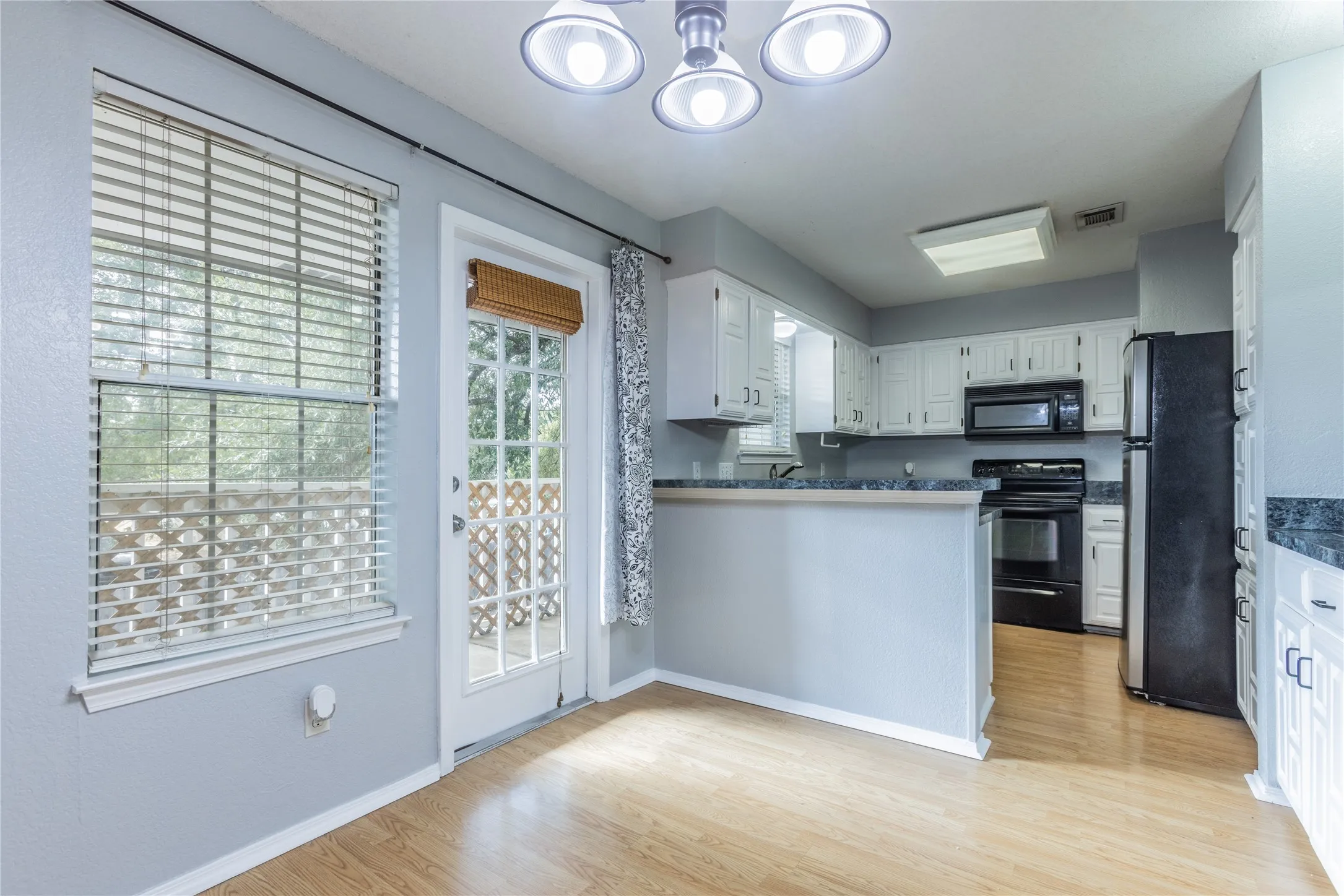 Kitchen with white cabinetry, black appliances, dark countertops, and wood-finish flooring