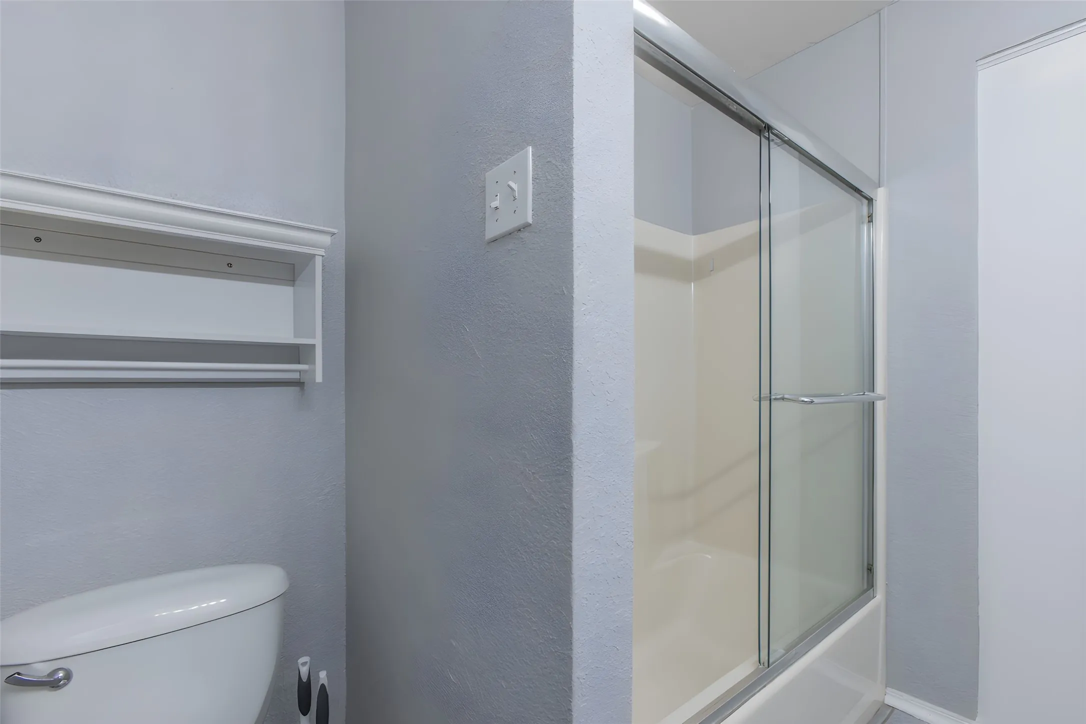 Bathtub with a sliding glass enclosure, integrated shelving, and a toilet