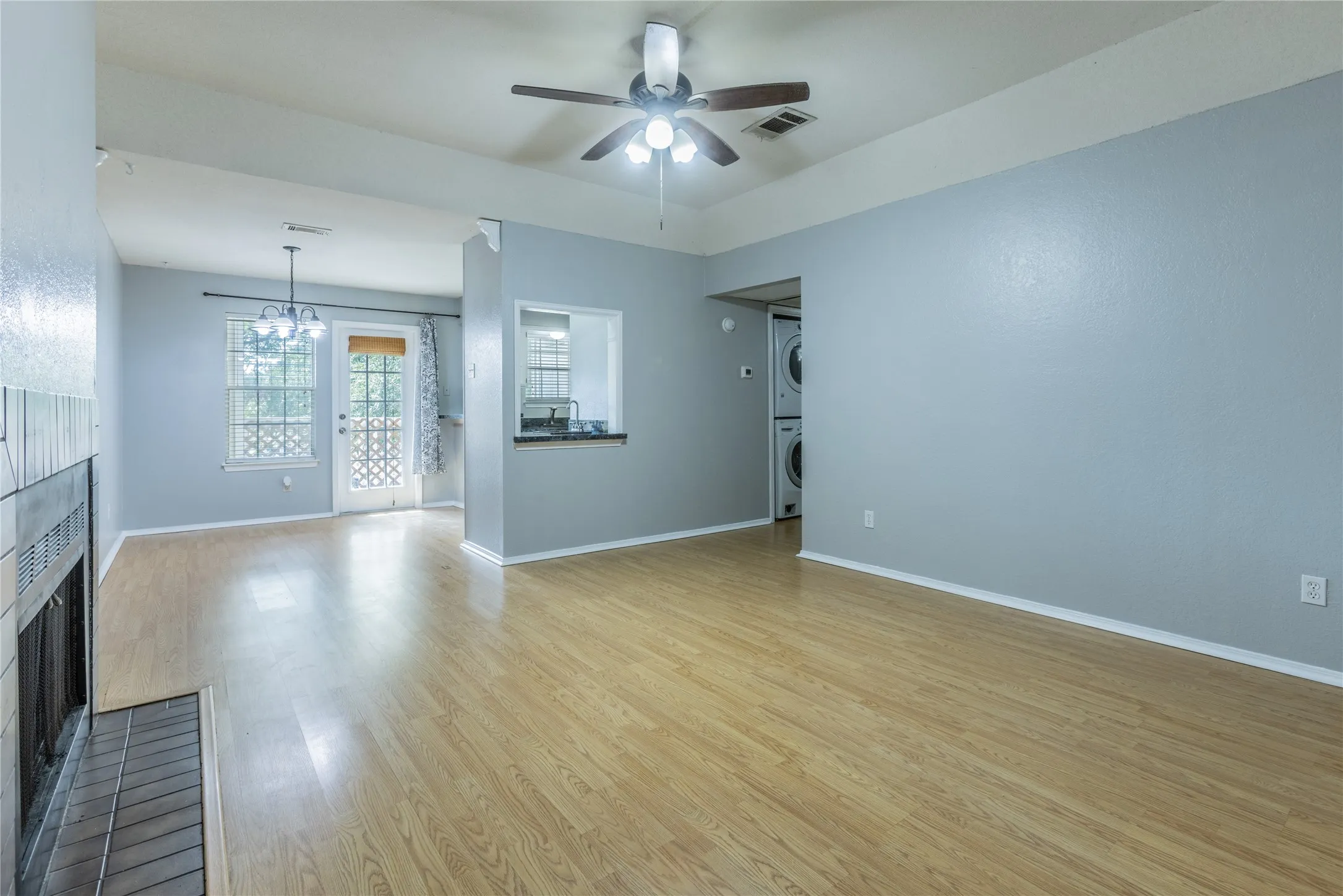 Vaulted ceiling, wood-finish flooring, fireplace with tile surround, built-in pass-through window, and stacked laundry appliances