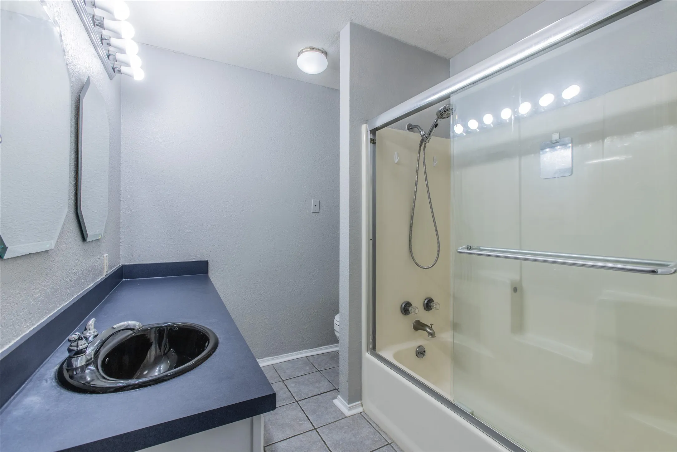 Bathroom with tile flooring, a dark countertop vanity, black oval sink, and a combination shower/tub with sliding glass doors
