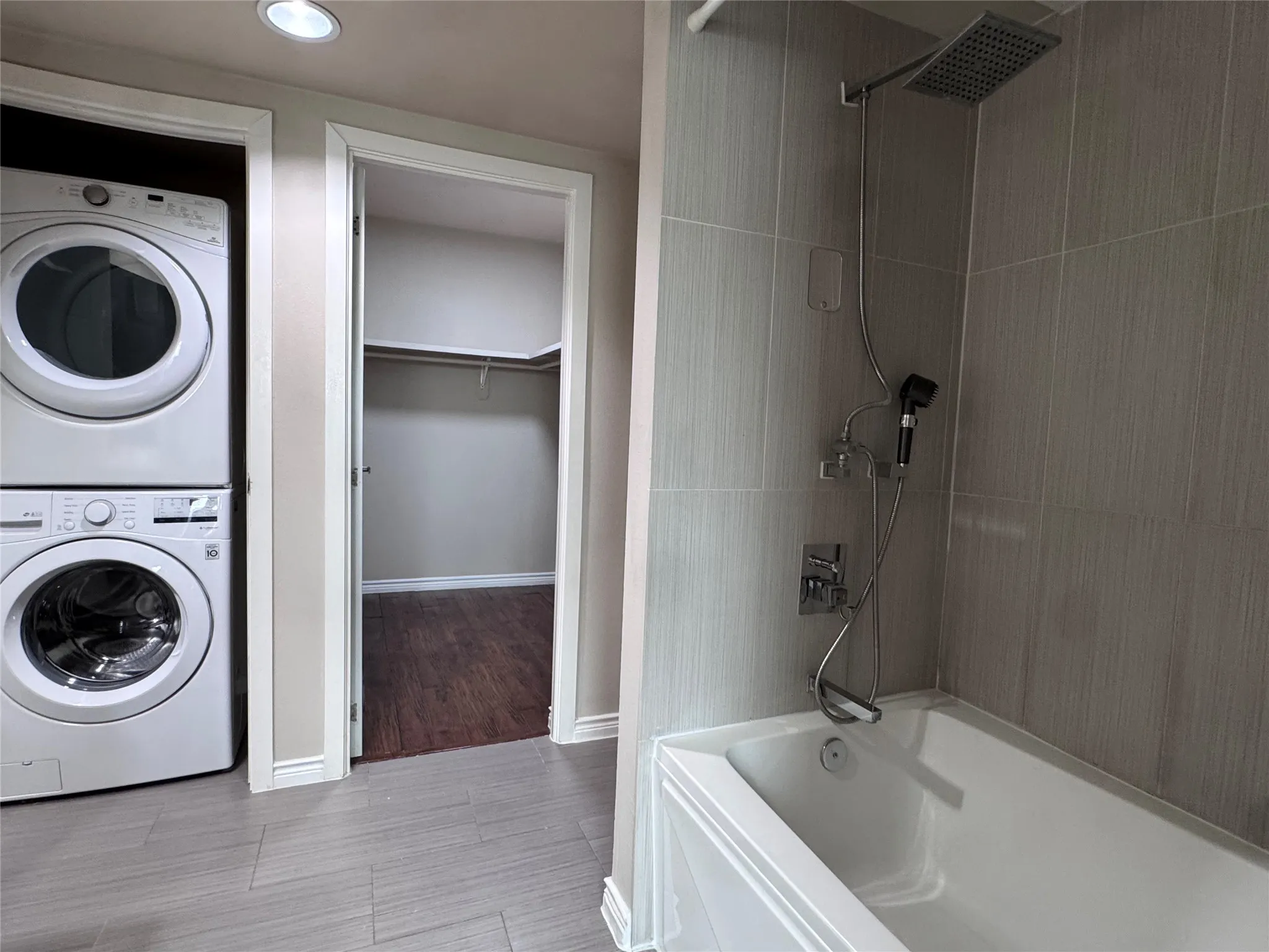 Stacked laundry appliances, recessed lighting, walk-in closet, tiled shower surround, and a rain showerhead