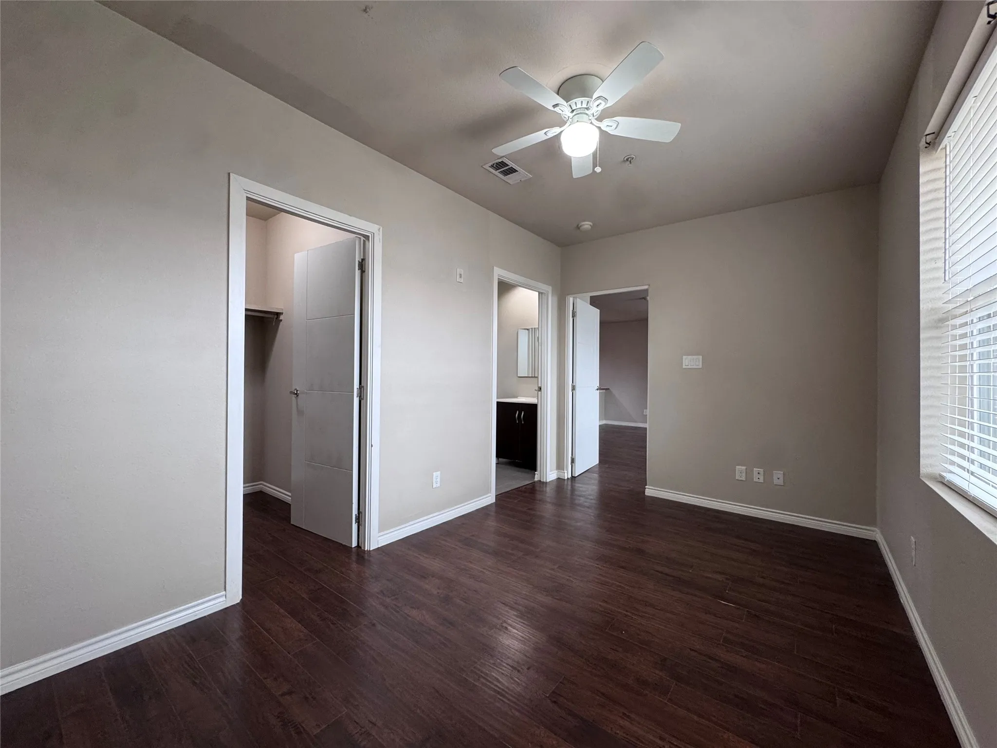 Wood-finish flooring, ceiling fan, window with blinds, and white trim throughout