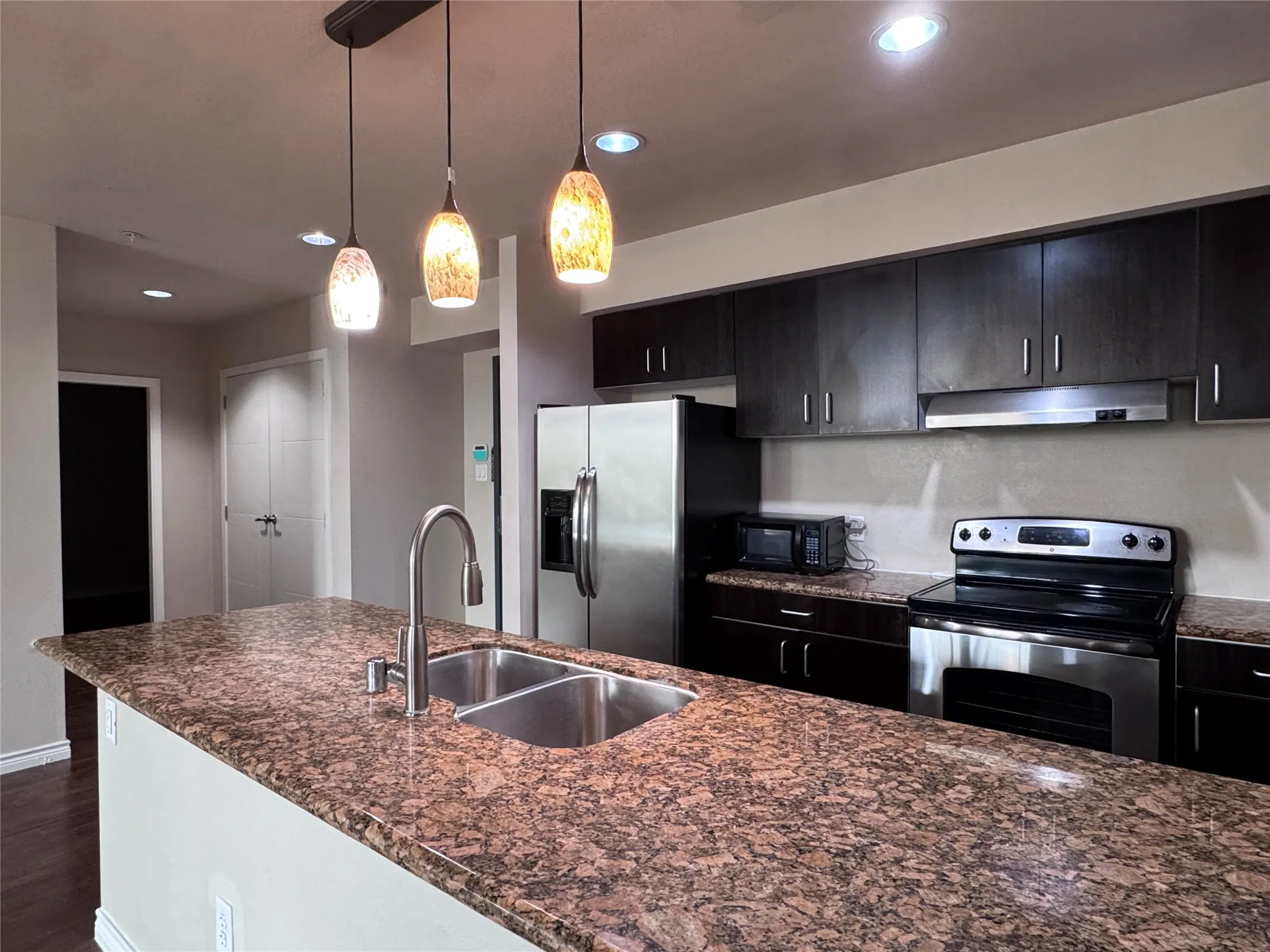 Kitchen featuring an island with double basin sink, stainless steel appliances, dark wood-finish cabinetry, recessed lighting, and pendant lighting