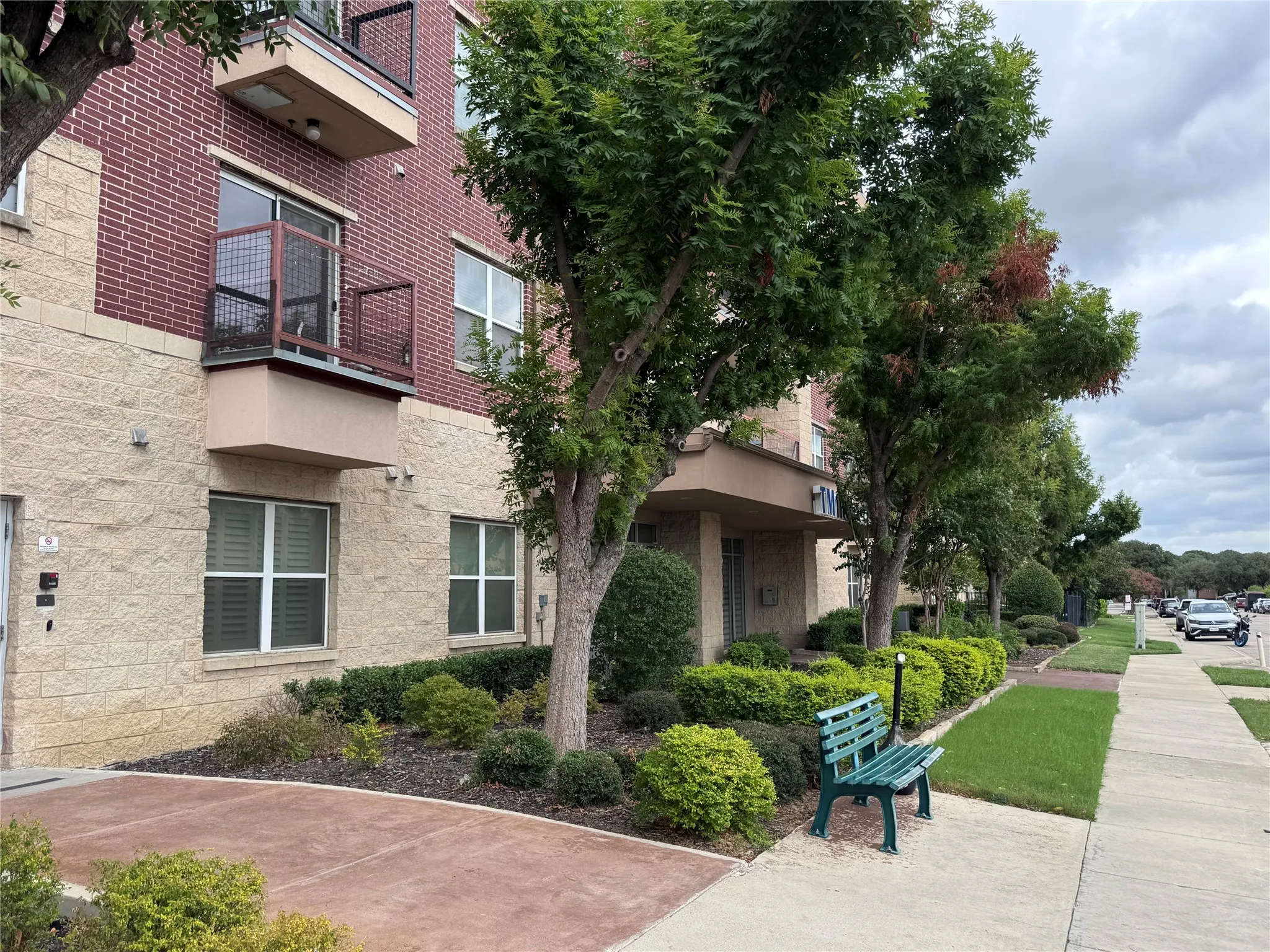 Brick and stone exterior with balconies, mature trees, and landscaped shrubbery