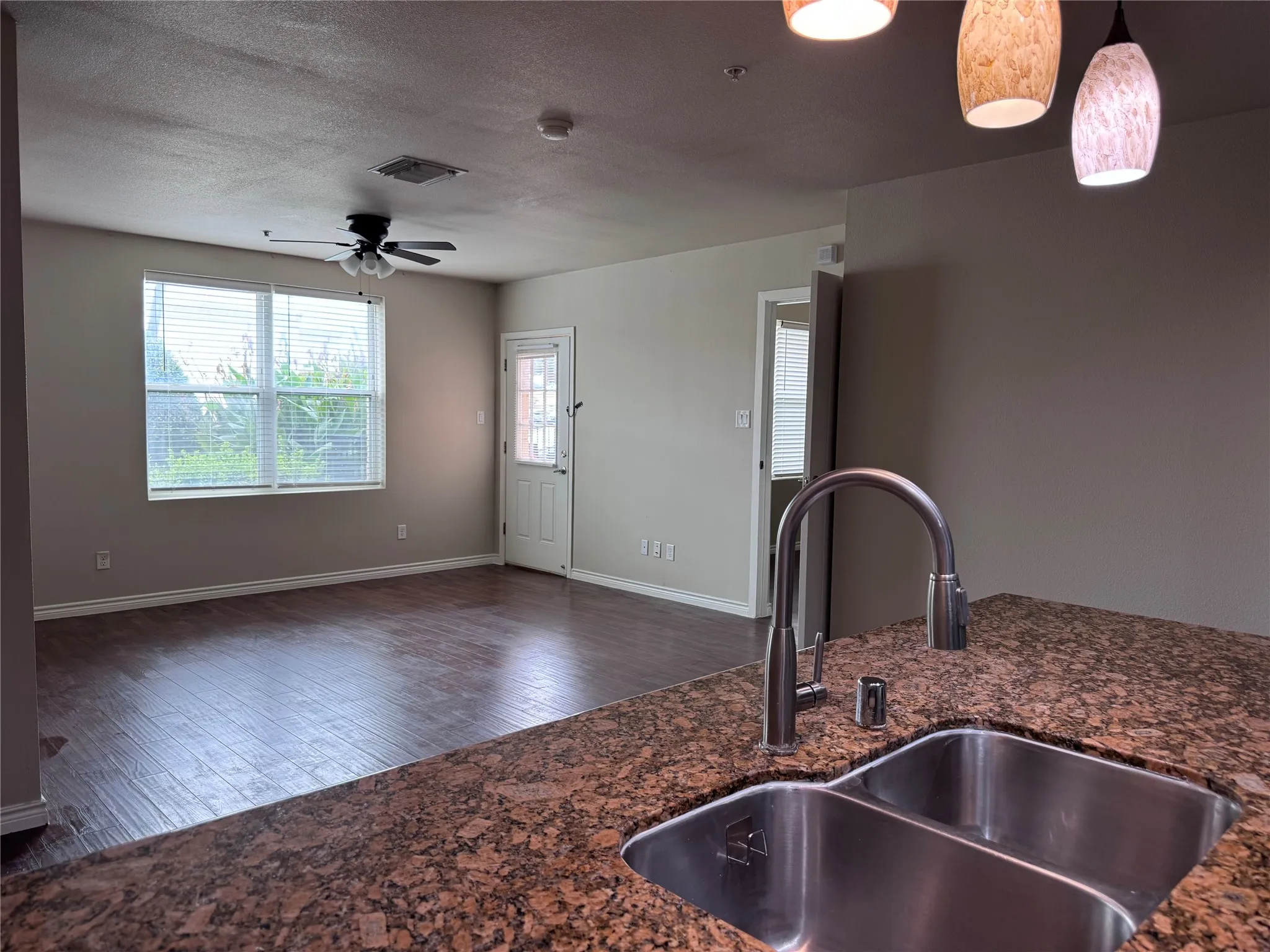Kitchen featuring a double basin stainless steel sink with a high-arc faucet, granite countertop, and pendant lighting
