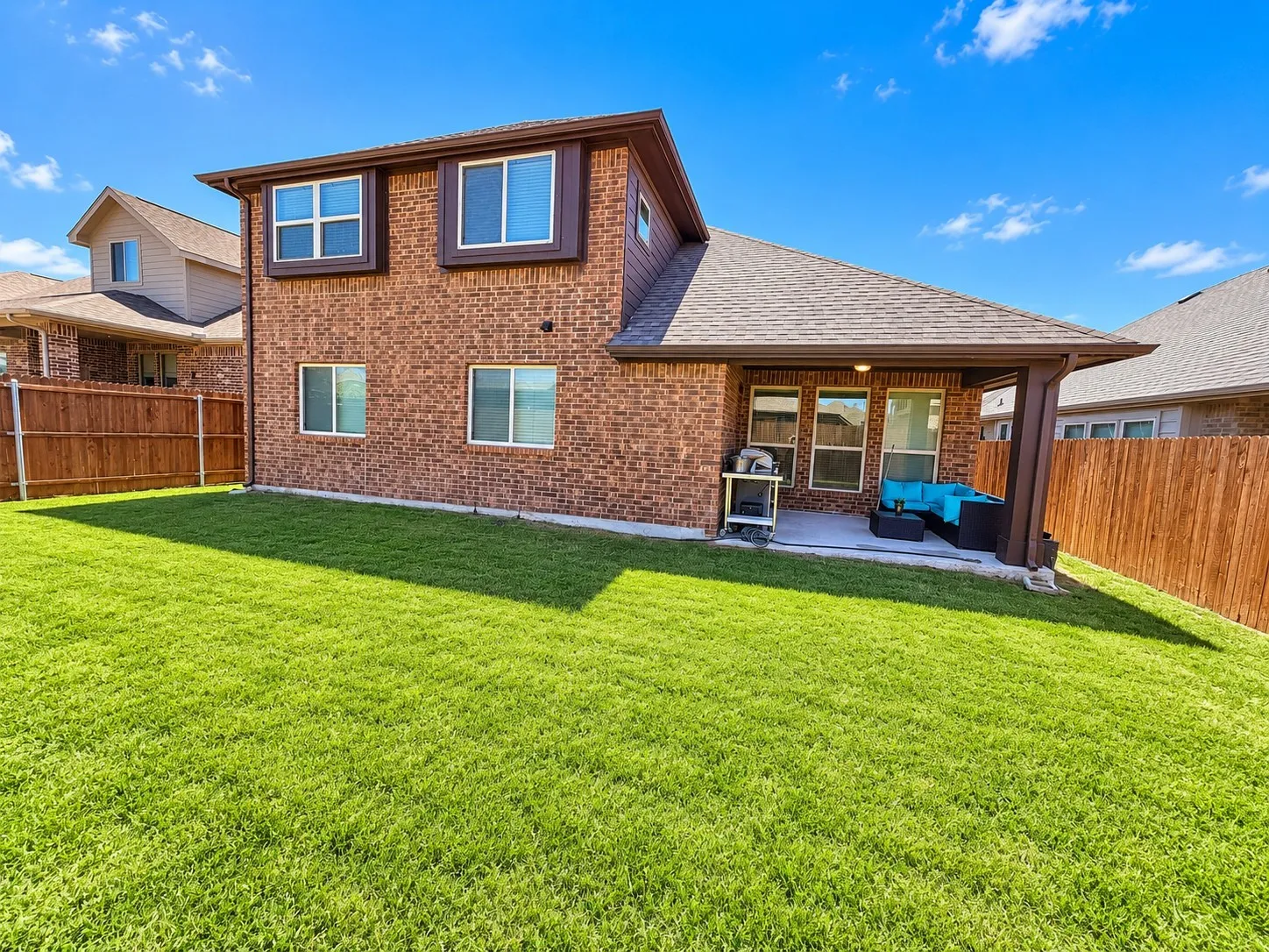 Brick exterior with brown trim, covered patio, and fenced yard