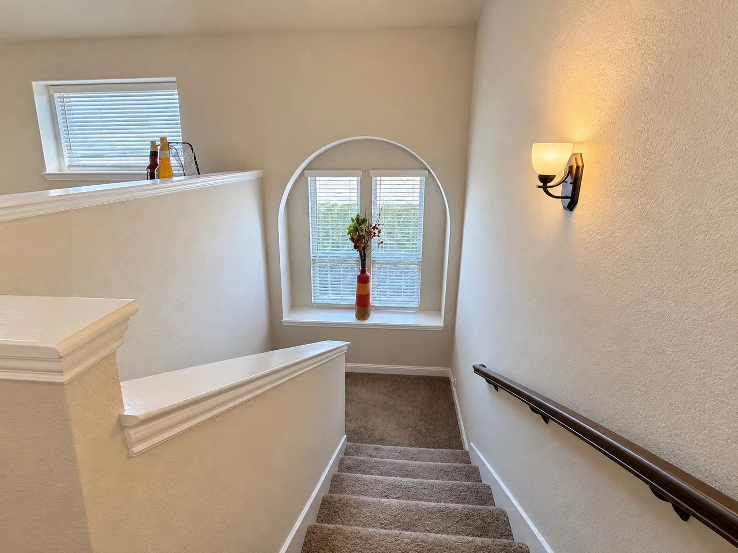 Carpeted staircase with a wood-finish handrail and a wall-mounted sconce
