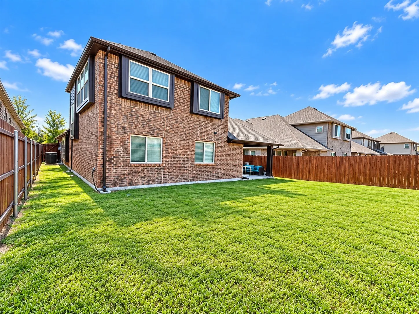 Expansive backyard featuring a manicured lawn, full privacy fencing, and a covered patio