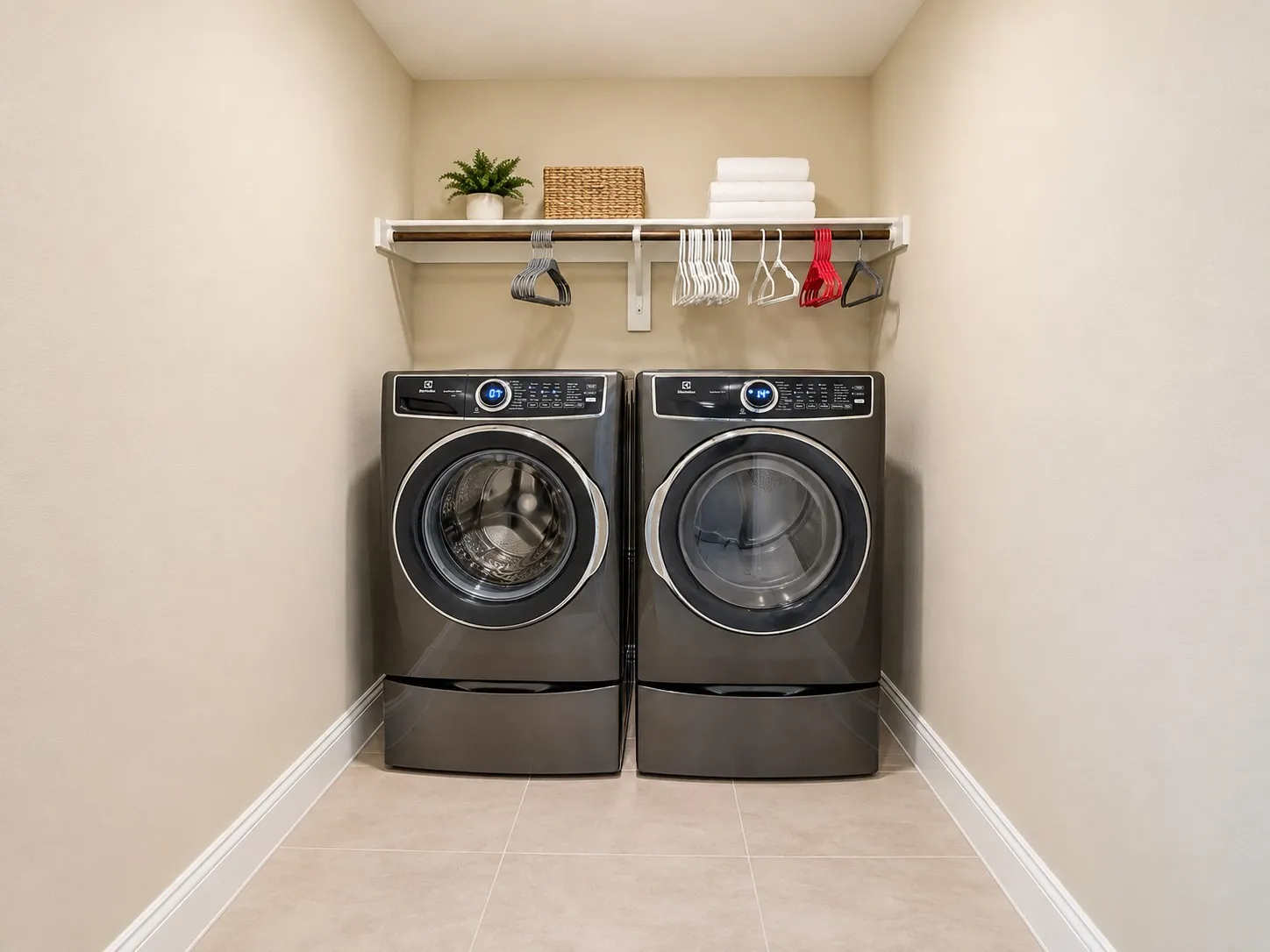 Compact laundry area featuring light-toned walls, tile flooring, and a white mounted shelf with a hanging rod