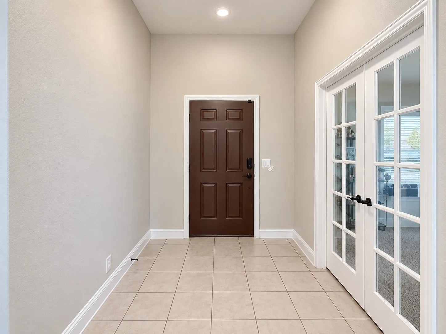 Recessed lighting illuminating a tiled entryway with a paneled door, complemented by French doors featuring multiple lites and matte black hardware