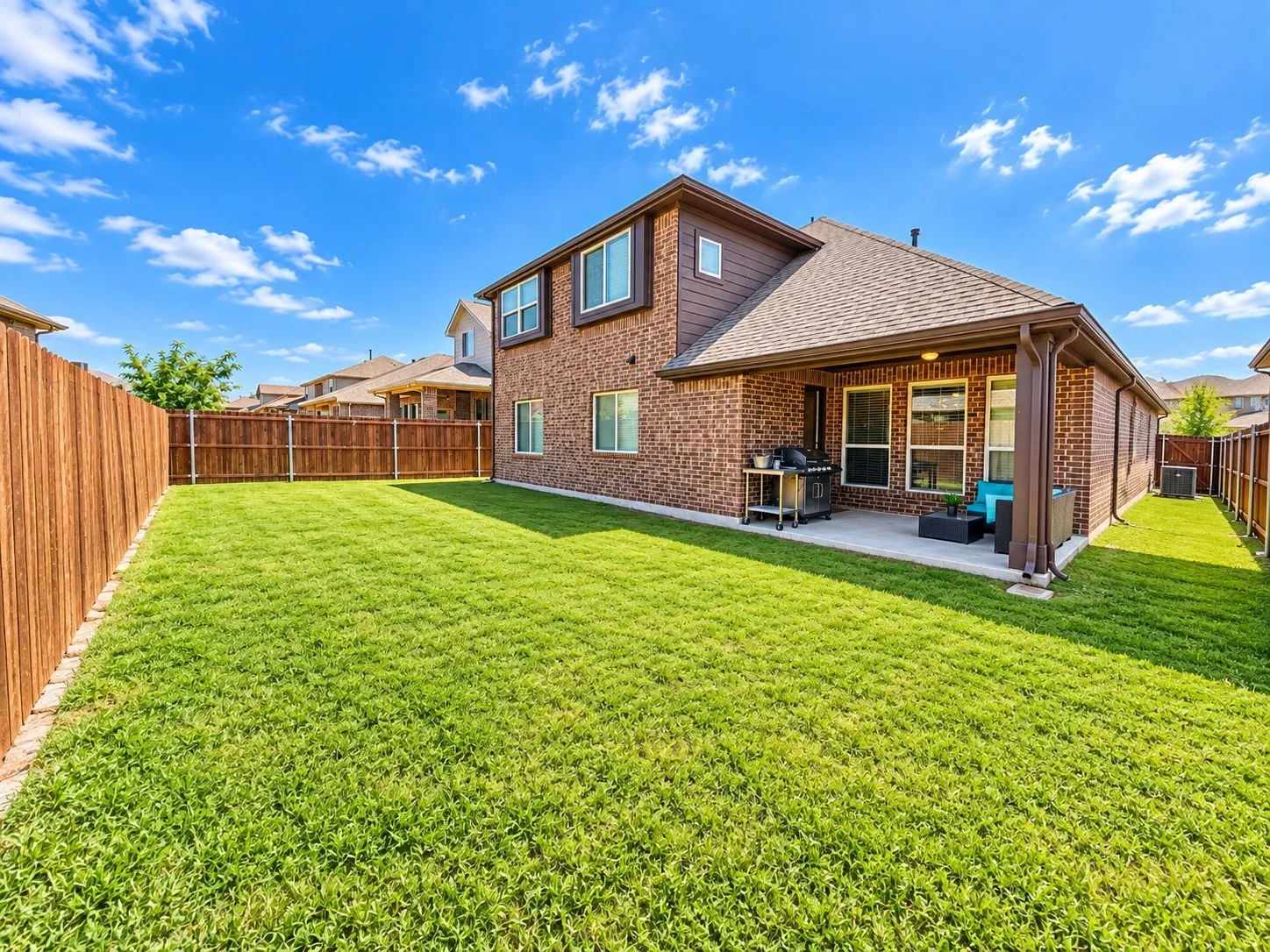 Expansive green lawn, a covered patio, brick exterior, and a privacy fence