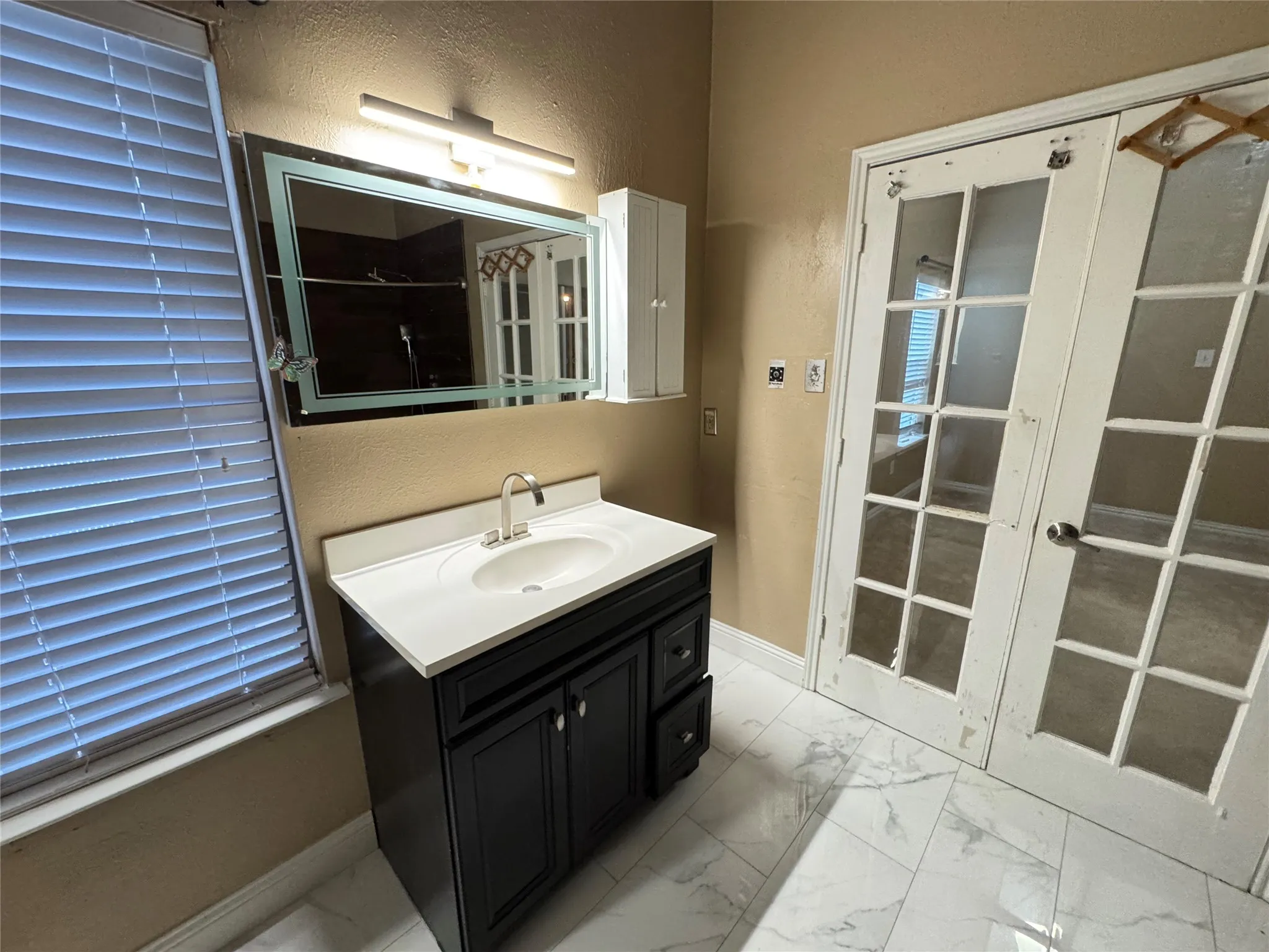 White tile flooring, a dark wood-finish vanity with a white countertop, and an illuminated wall mirror