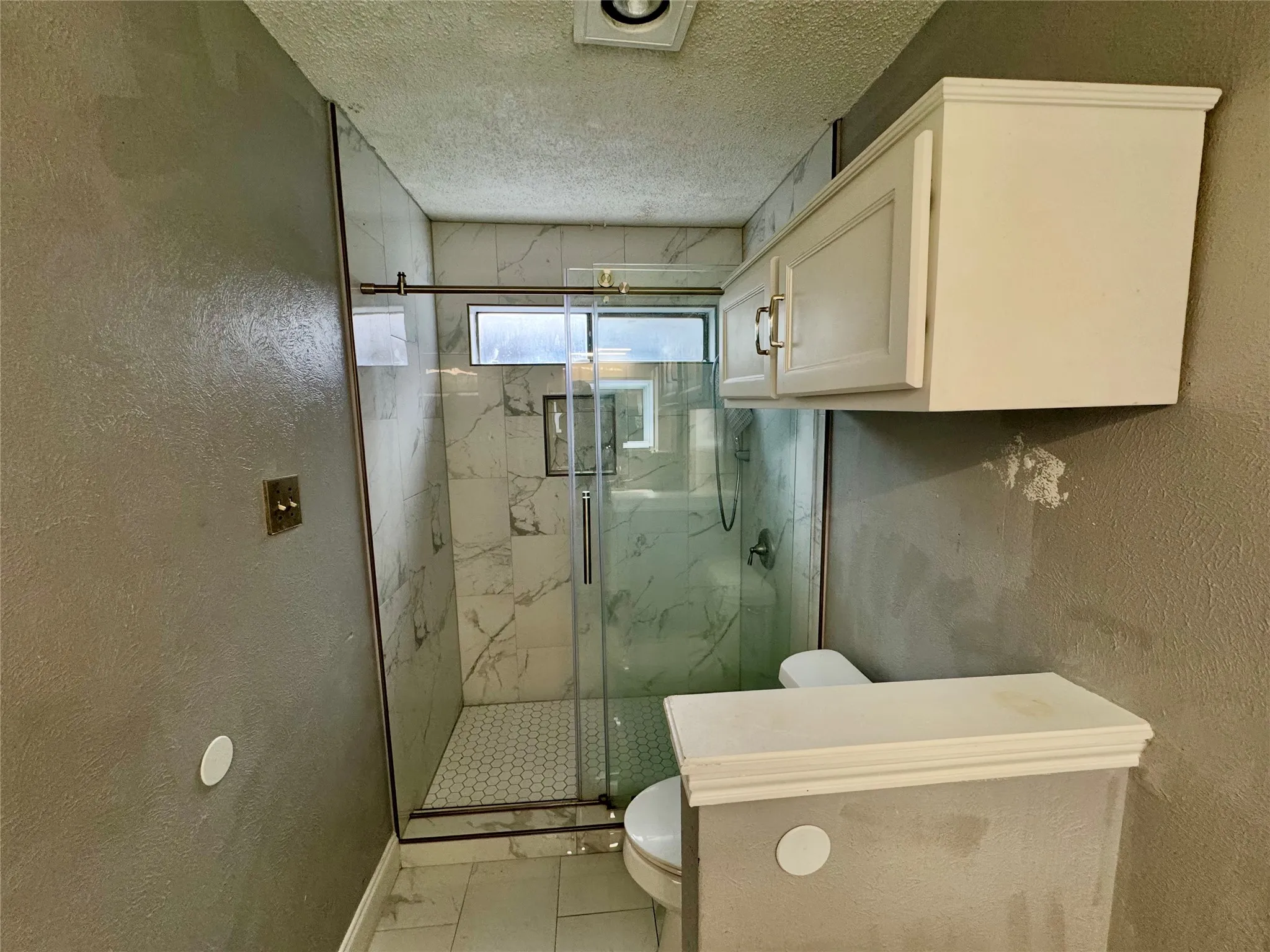 Walk-in shower with clear glass enclosure, white hexagon tile shower floor, and a built-in shower niche