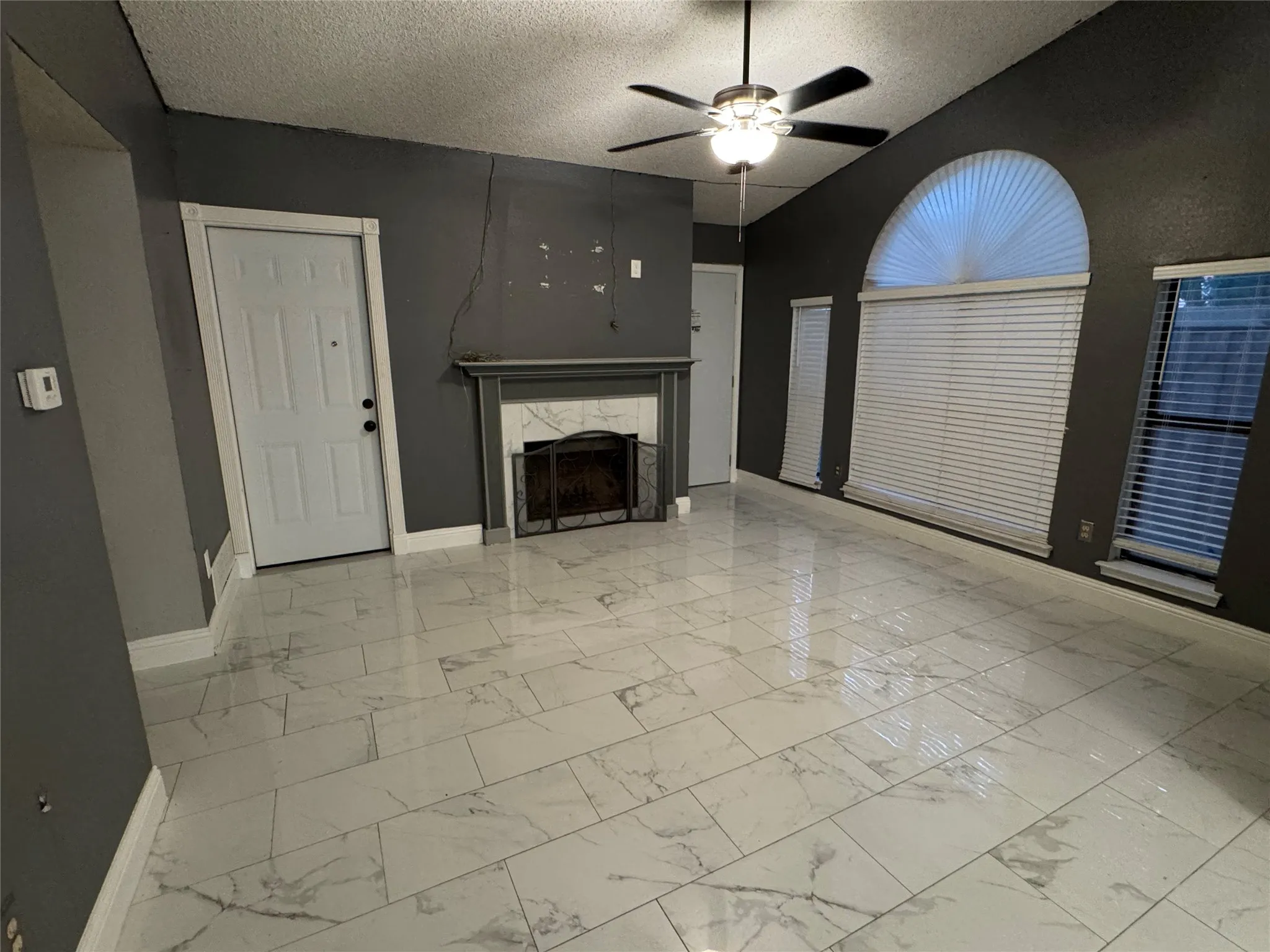 White large-format tile flooring, a fireplace with a white mantel, and a decorative fireplace screen