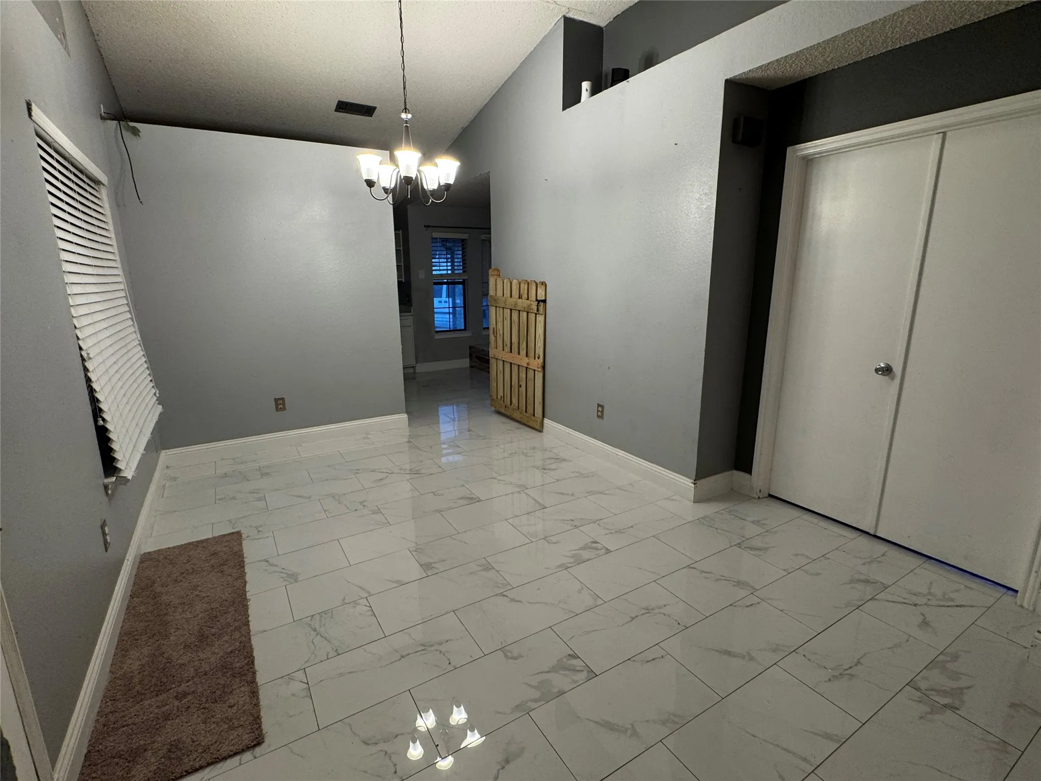 White tiled flooring with subtle veining, interior window with white blinds, and a built-in chandelier