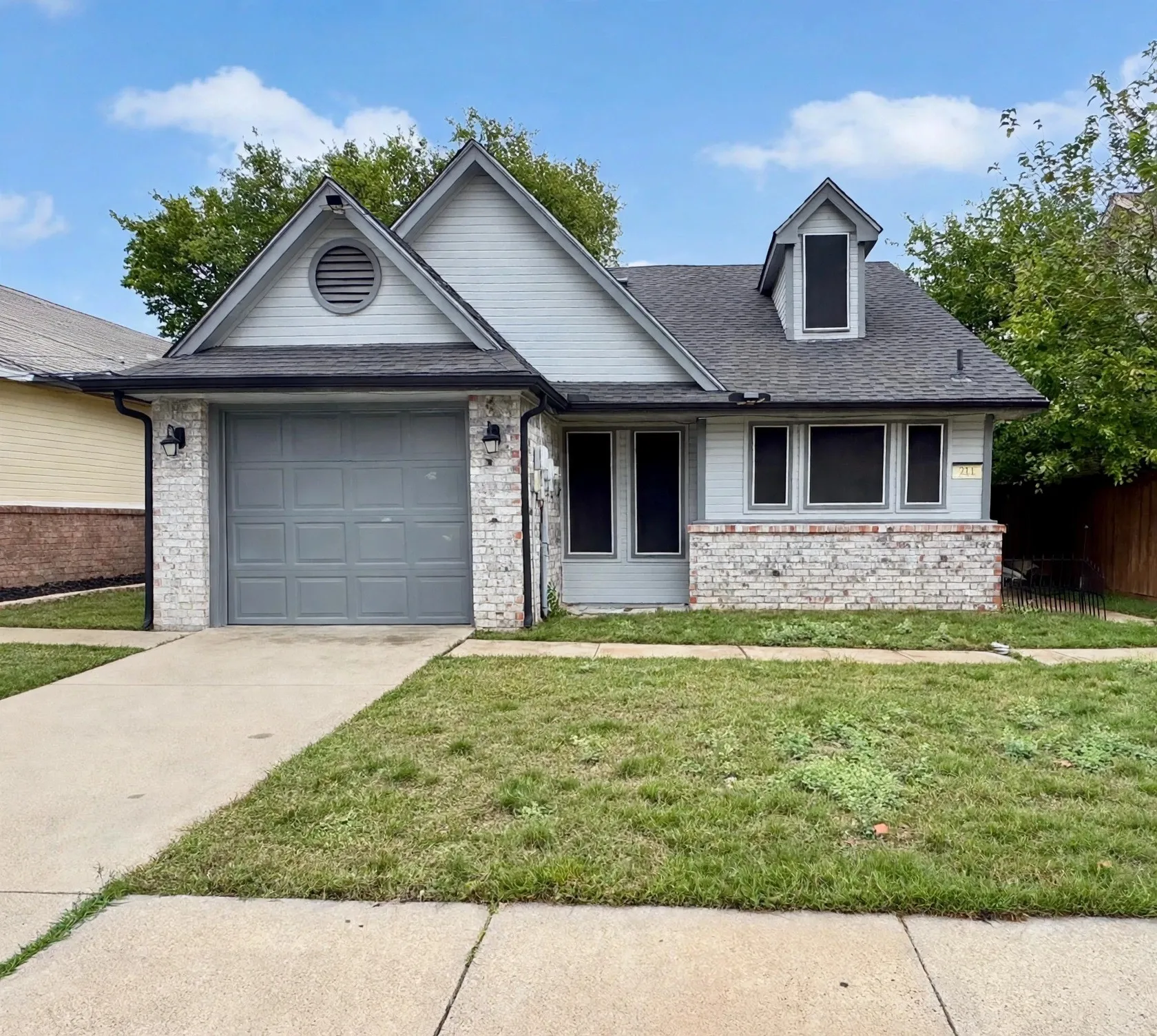 Exterior featuring a gray garage door, white brick facade, and gray siding