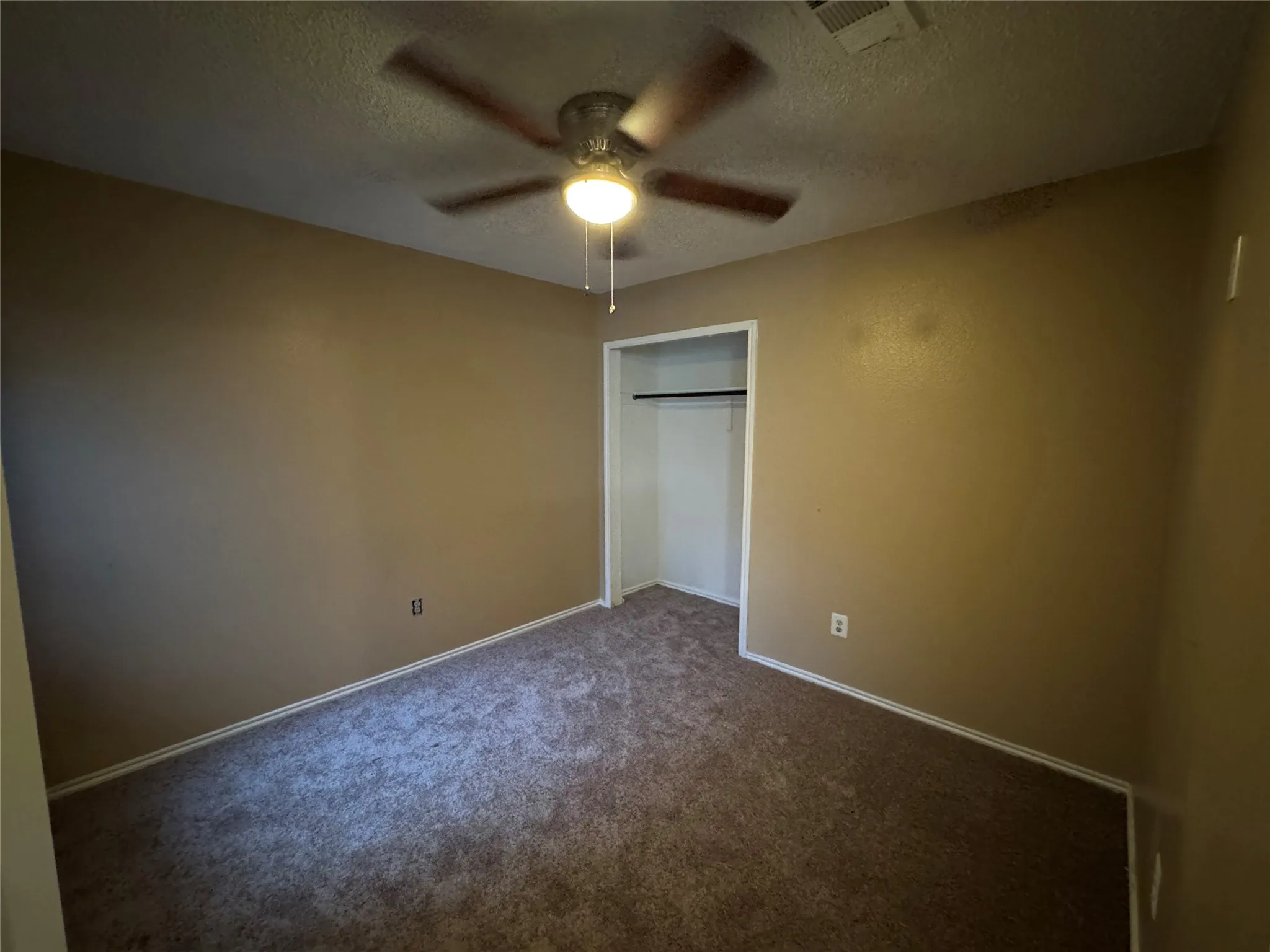 Brown carpeting, ceiling fan with integrated lighting, and an open closet with hanging rod