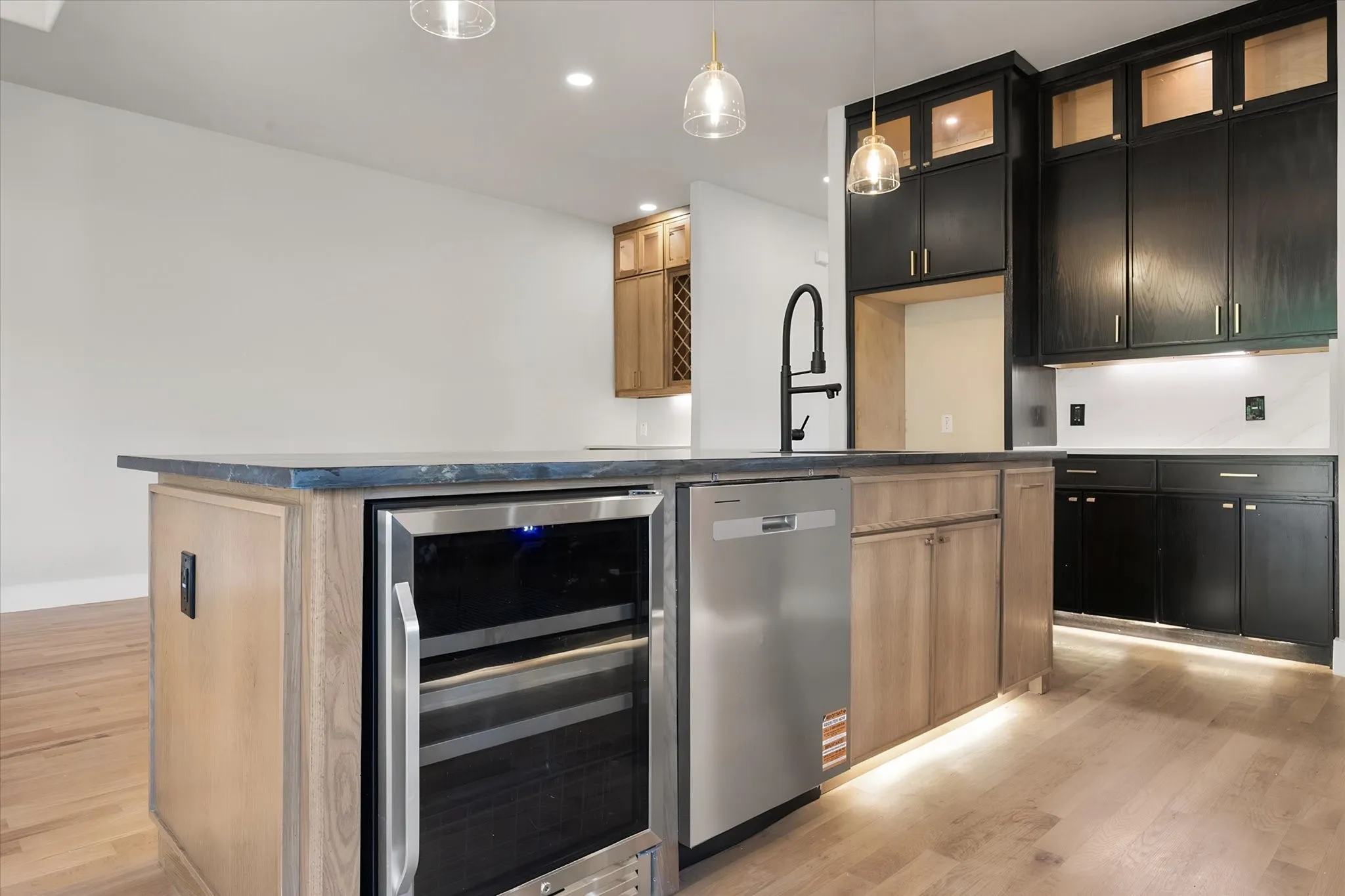 Expansive kitchen island with a built-in beverage refrigerator, stainless steel dishwasher, and a matte black faucet
