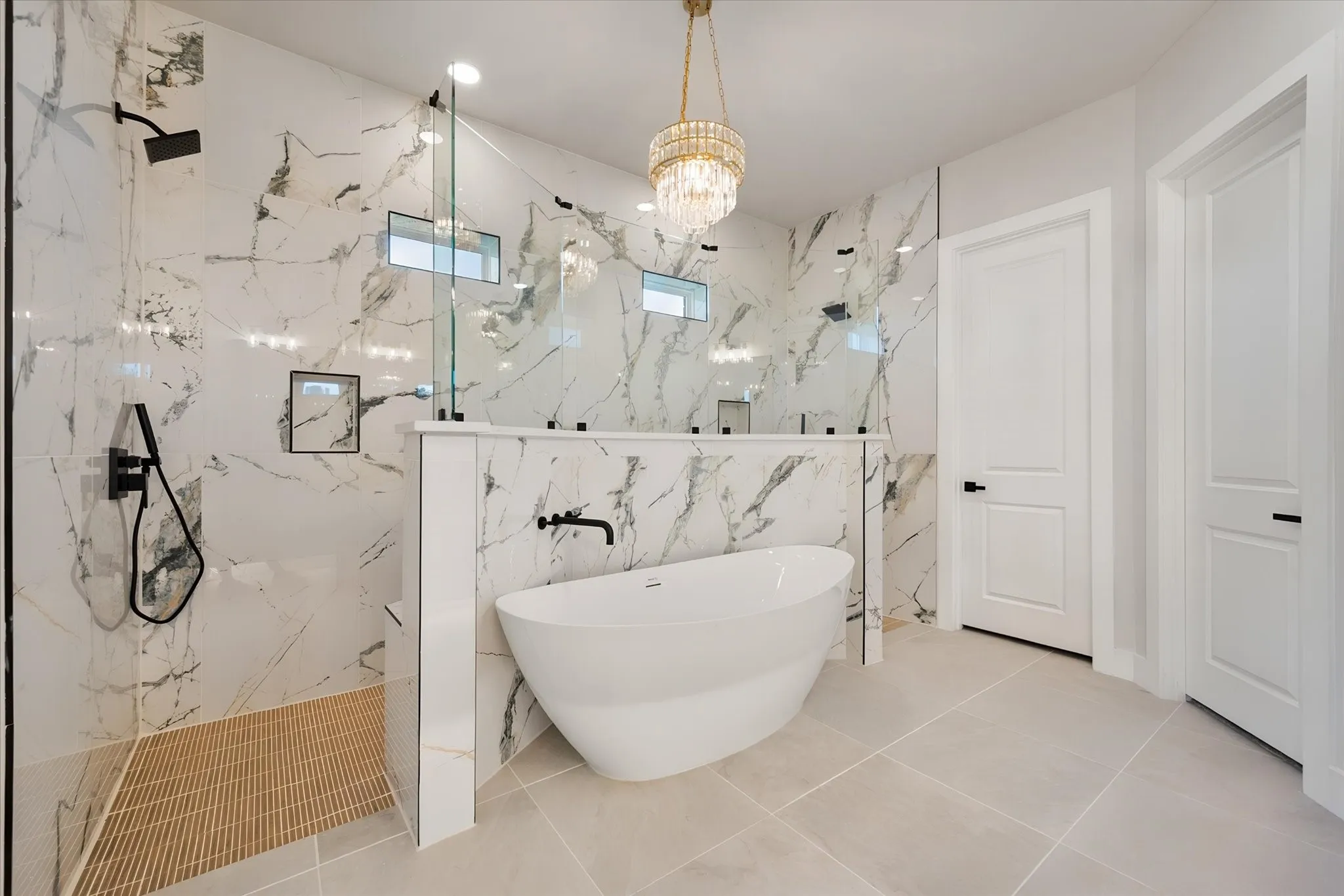 Spacious bathroom featuring a freestanding tub, large walk-in shower with glass enclosure, striking marble-look wall tile, and a decorative chandelier