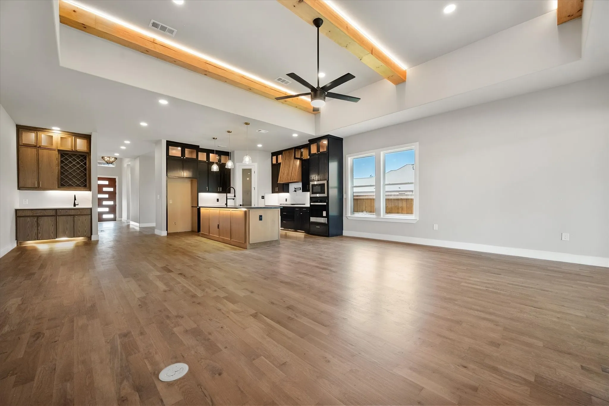 Vaulted ceilings with exposed wood beams, wood-finish flooring, a kitchen island with pendant lighting, built-in cabinetry with a wine rack, and a modern ceiling fan