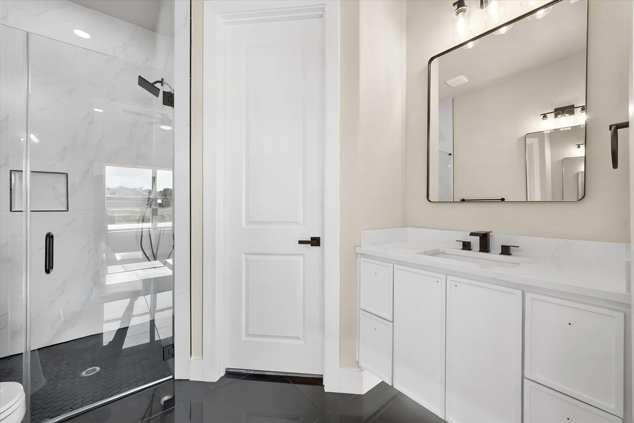 Glass-enclosed shower with a black tile floor, white tiled walls, and a recessed niche
