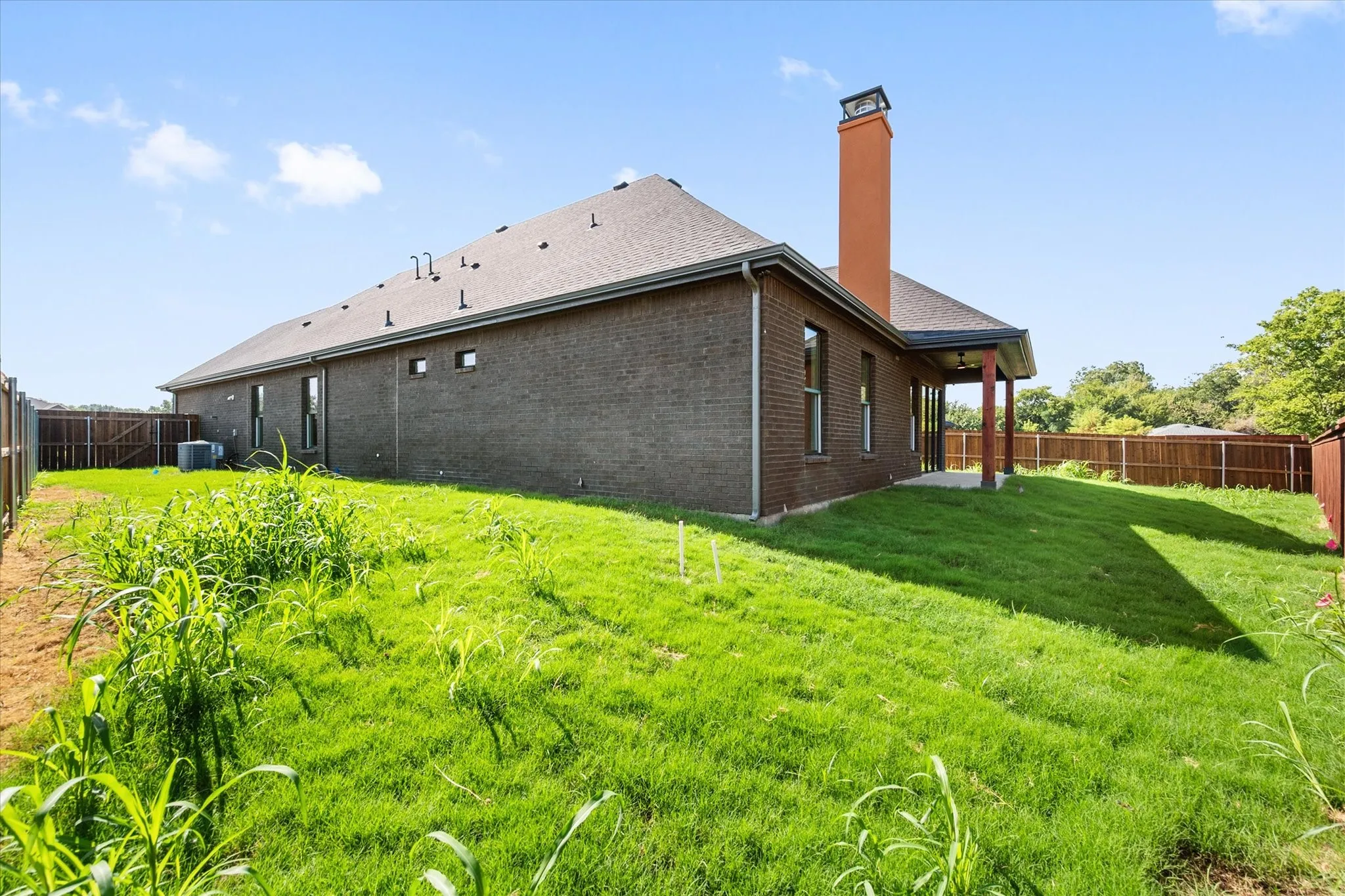 Brick exterior with a prominent chimney, dark shingle roof, privacy fencing, and a covered back patio