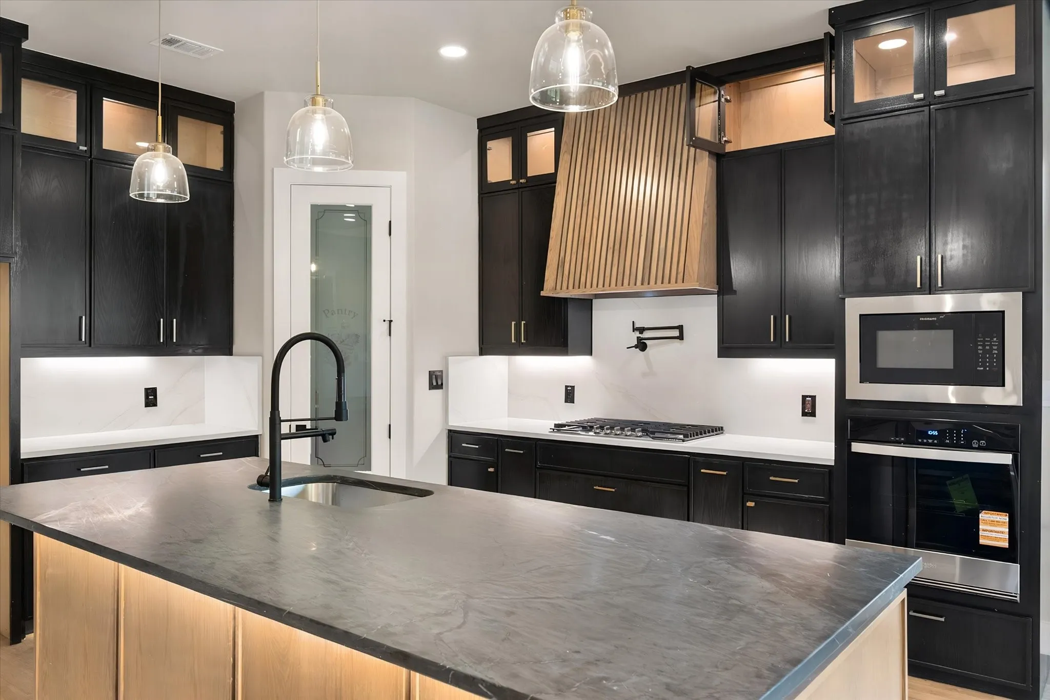 Kitchen featuring black cabinetry, light wood-finish accents, and integrated stainless steel appliances