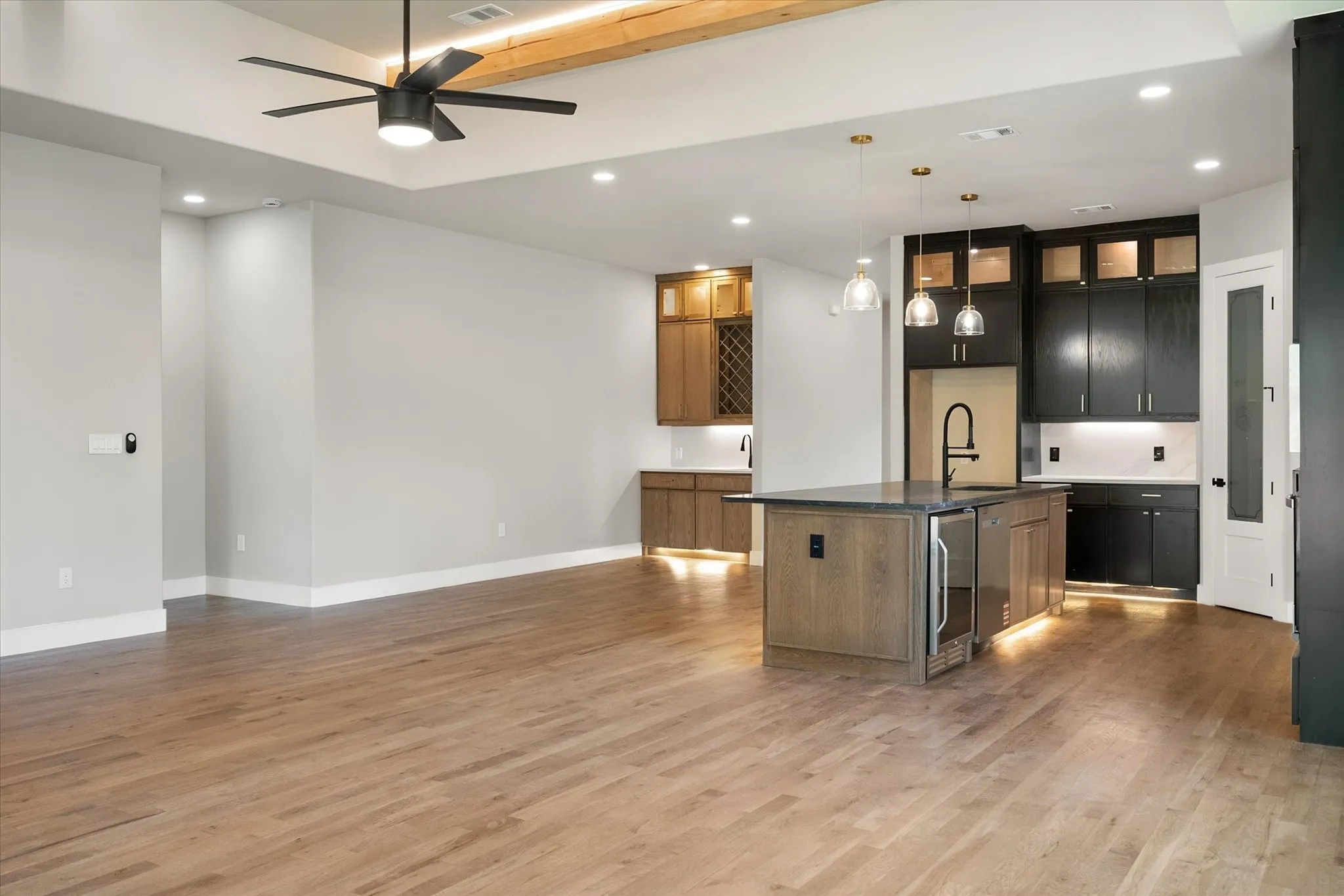 Wood-finish flooring throughout, tray ceiling with exposed wood beam, recessed lighting, and a modern ceiling fan