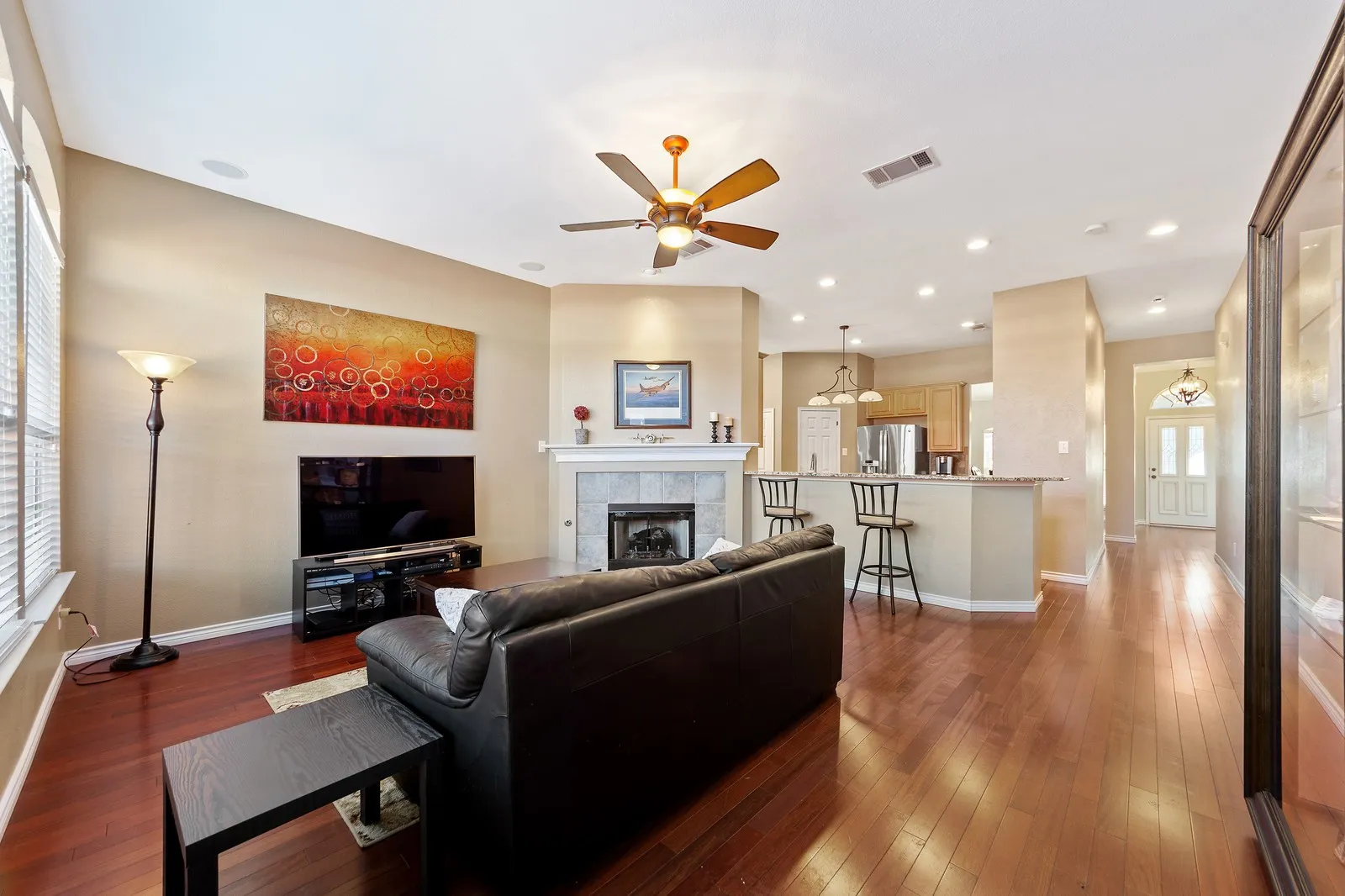 Wood-finish flooring throughout, featuring a fireplace with a stone surround and mantel, a ceiling fan, and recessed lighting