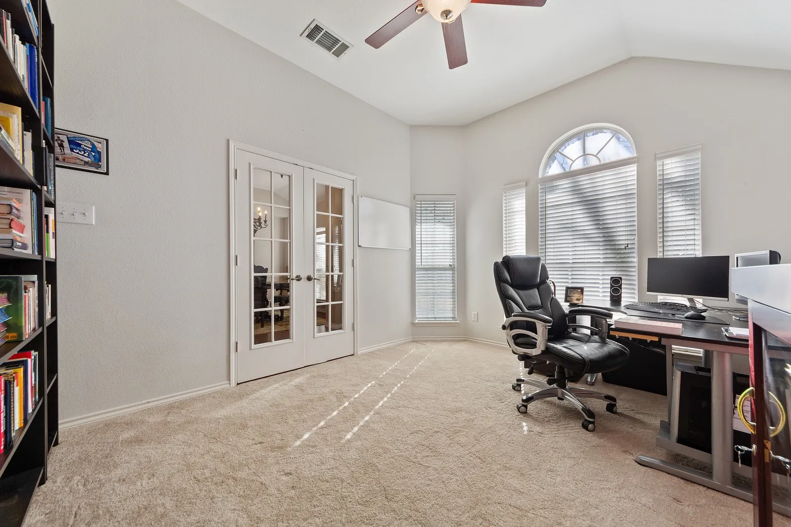 Vaulted ceiling with a ceiling fan, arched transom window, French doors, and carpet flooring
