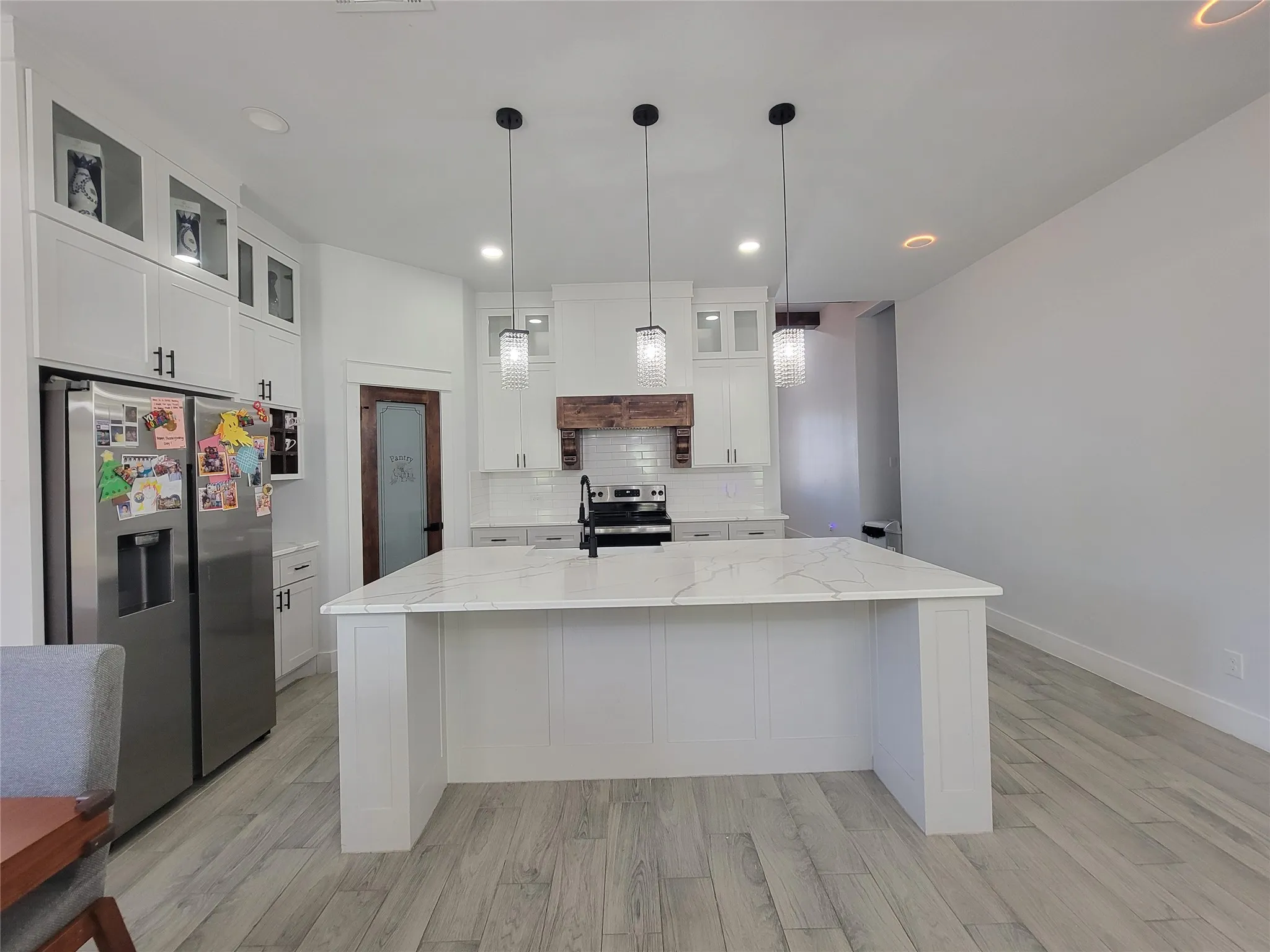 Spacious kitchen featuring a large central island with a light-toned countertop, white cabinetry with dark hardware, a tile backsplash, and light wood-finish flooring