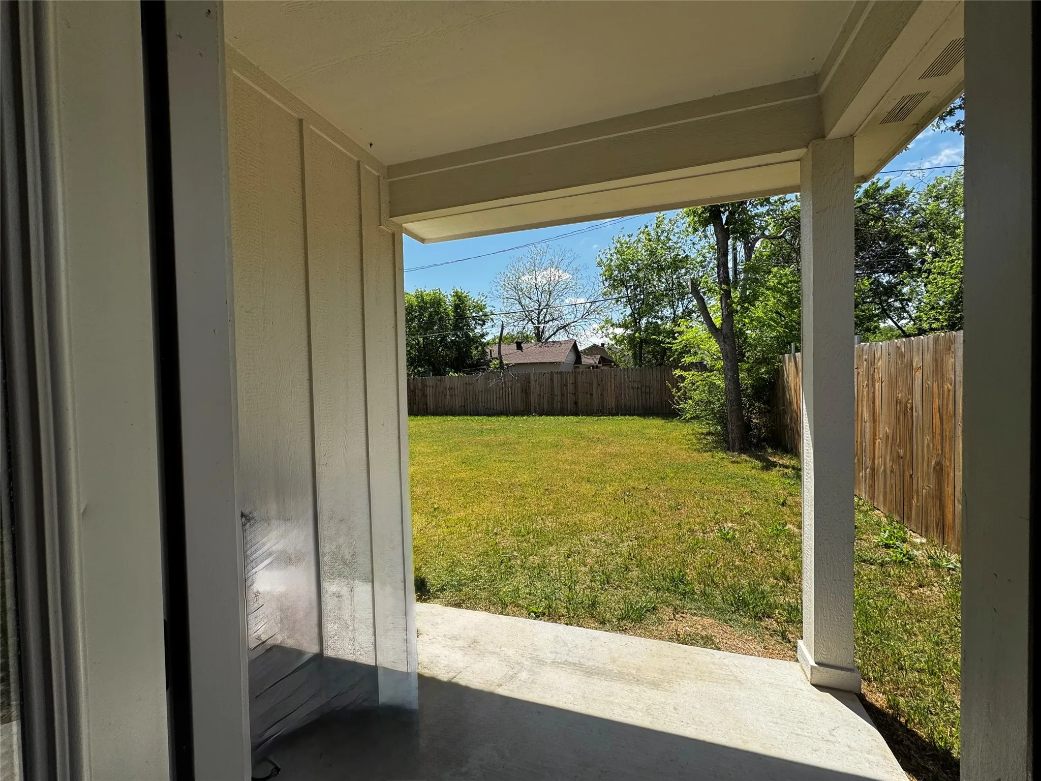 Covered patio with concrete flooring, overlooking a green lawn and wood fencing