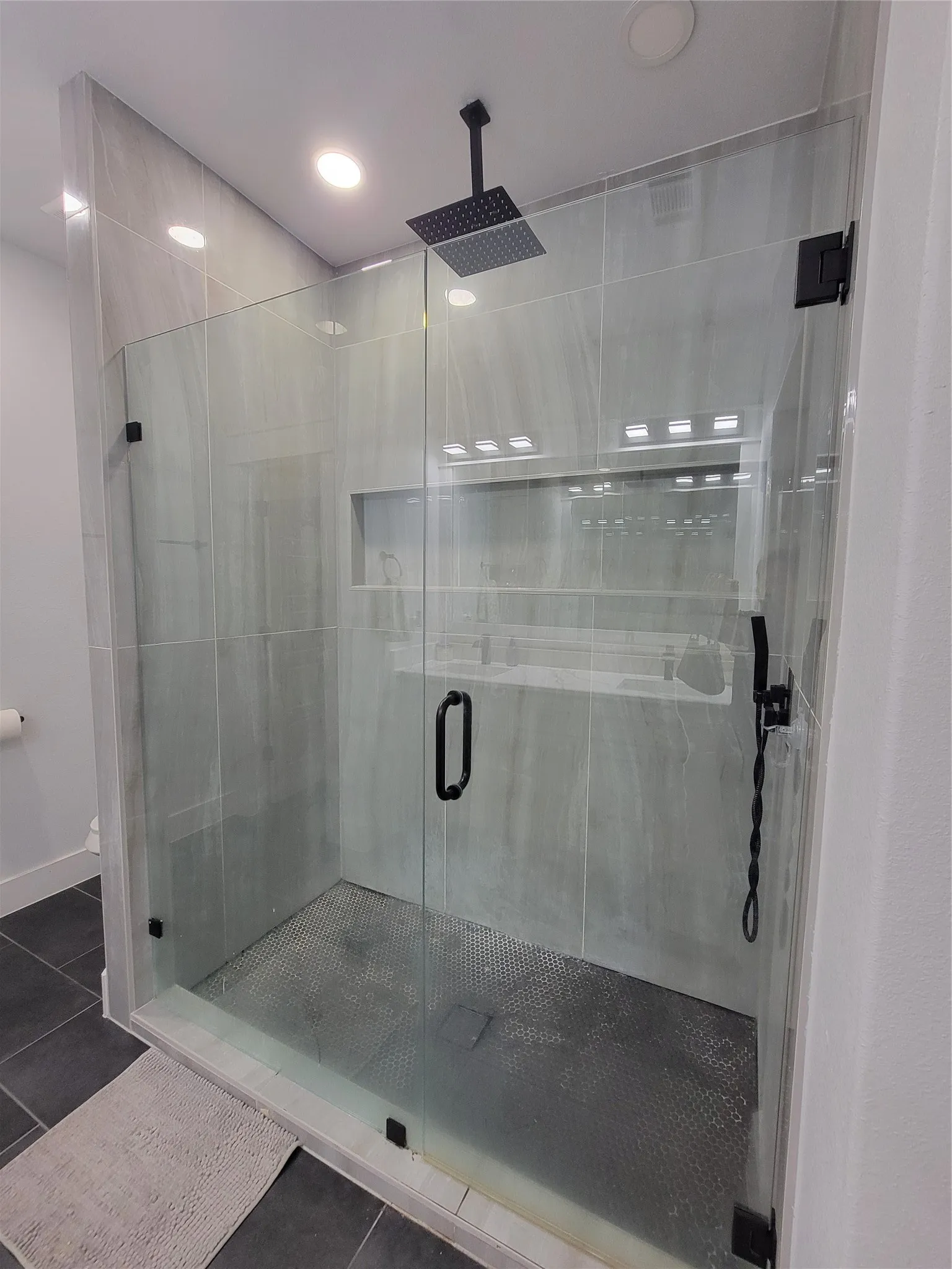 Enclosed shower with frameless glass, matte black hardware, rain shower head, and tiled walls