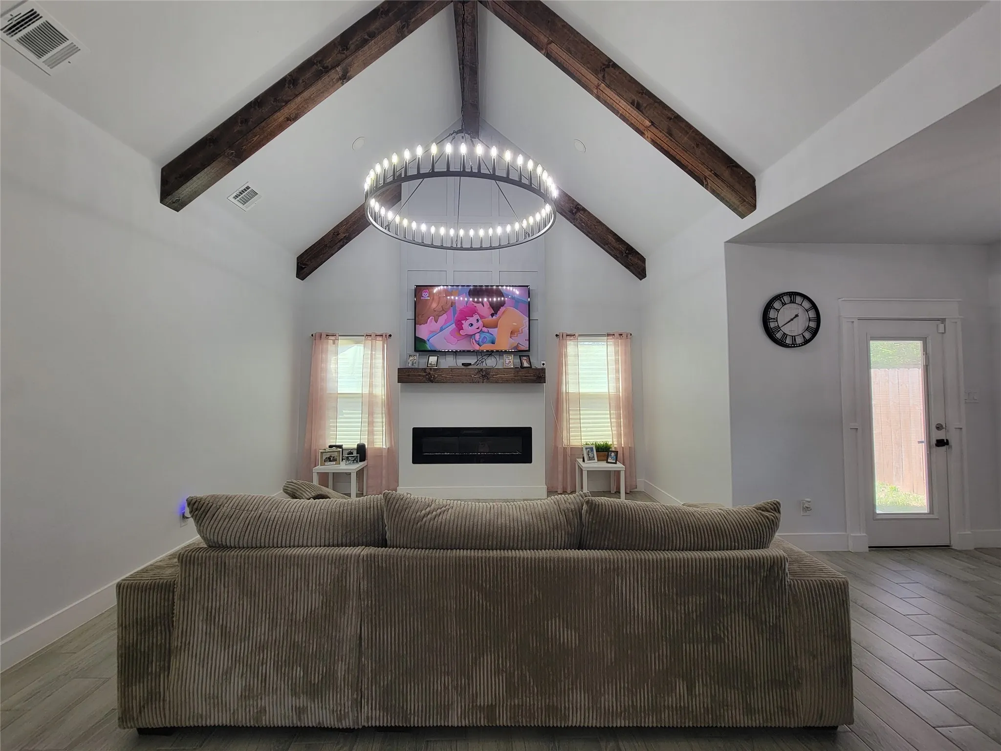 Vaulted ceiling with exposed wood beams, a contemporary chandelier, and a built-in electric fireplace with a wood-finish mantel