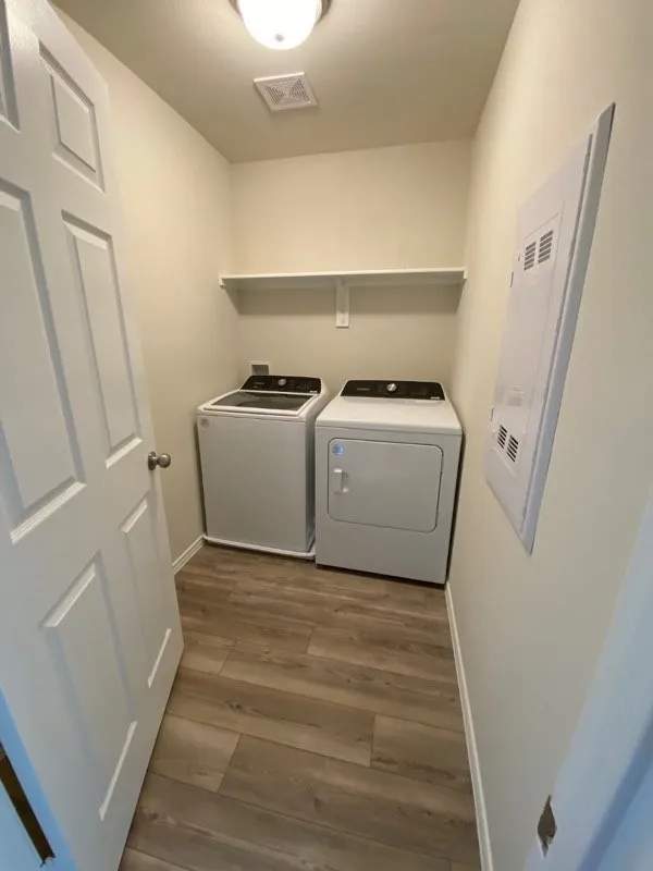 Laundry area featuring wood-finish flooring, a wall-mounted shelving unit, and overhead lighting