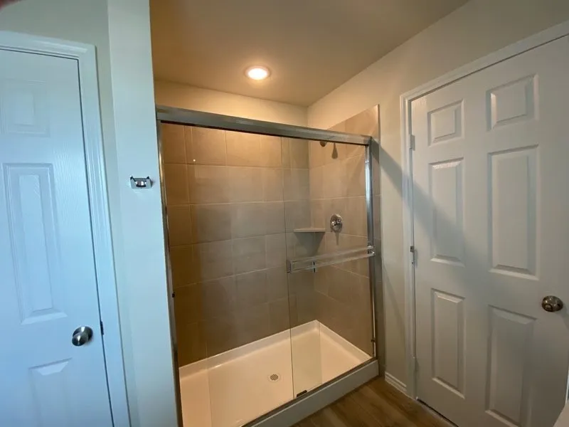 Walk-in shower with clear glass enclosure, tiled walls, and built-in corner shelf
