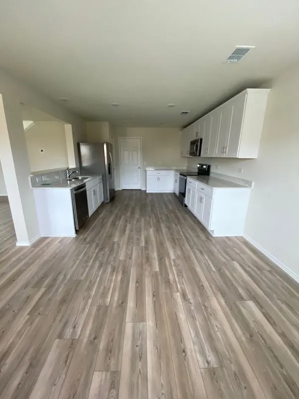 Expansive kitchen featuring wood-finish flooring, white cabinetry, integrated stainless steel appliances, and light-toned countertops