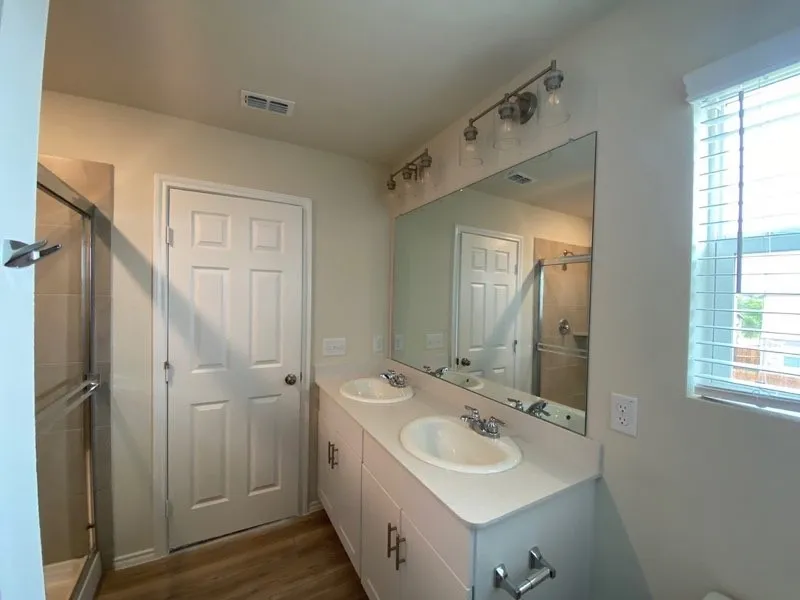 Dual vanity with integrated sinks, contemporary light fixture, large mirror, and wood-finish flooring