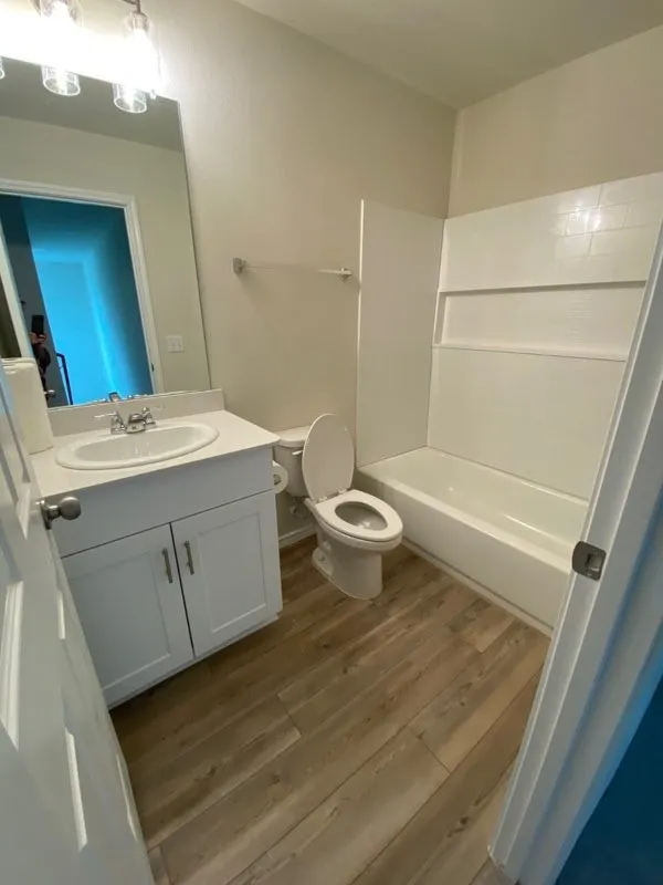 Bathroom featuring wood-finish flooring, a white vanity with cabinet storage, a white countertop, and a white bathtub with tile surround