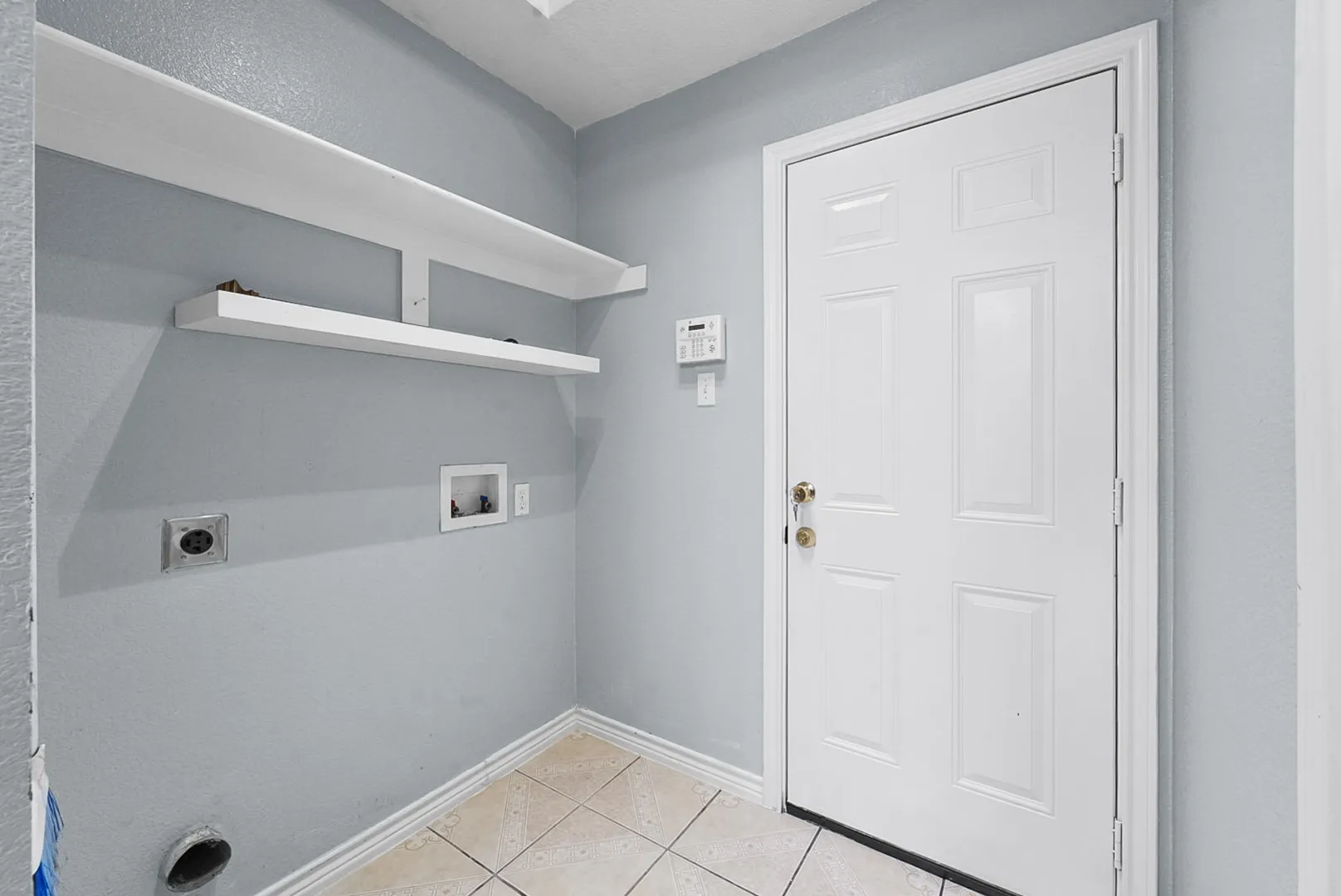 Utility area featuring tiled flooring, two white floating shelves, and a paneled entry door