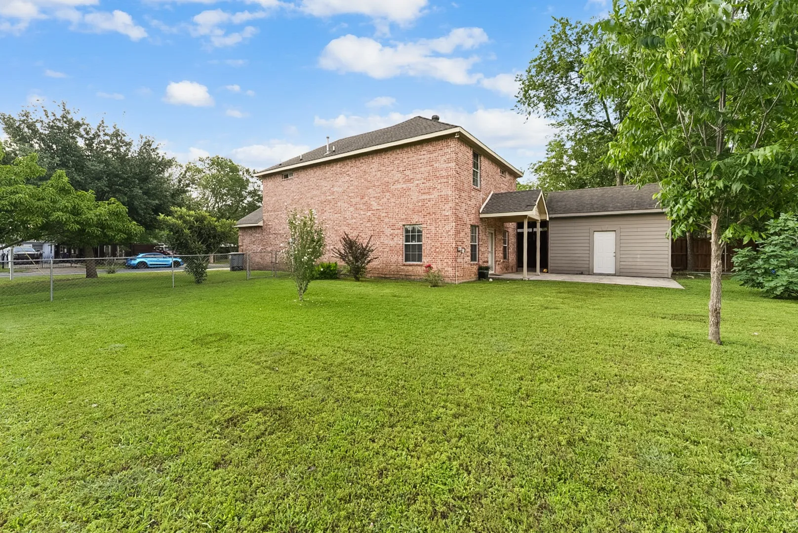 Expansive lawn area with mature trees and a brick exterior residence