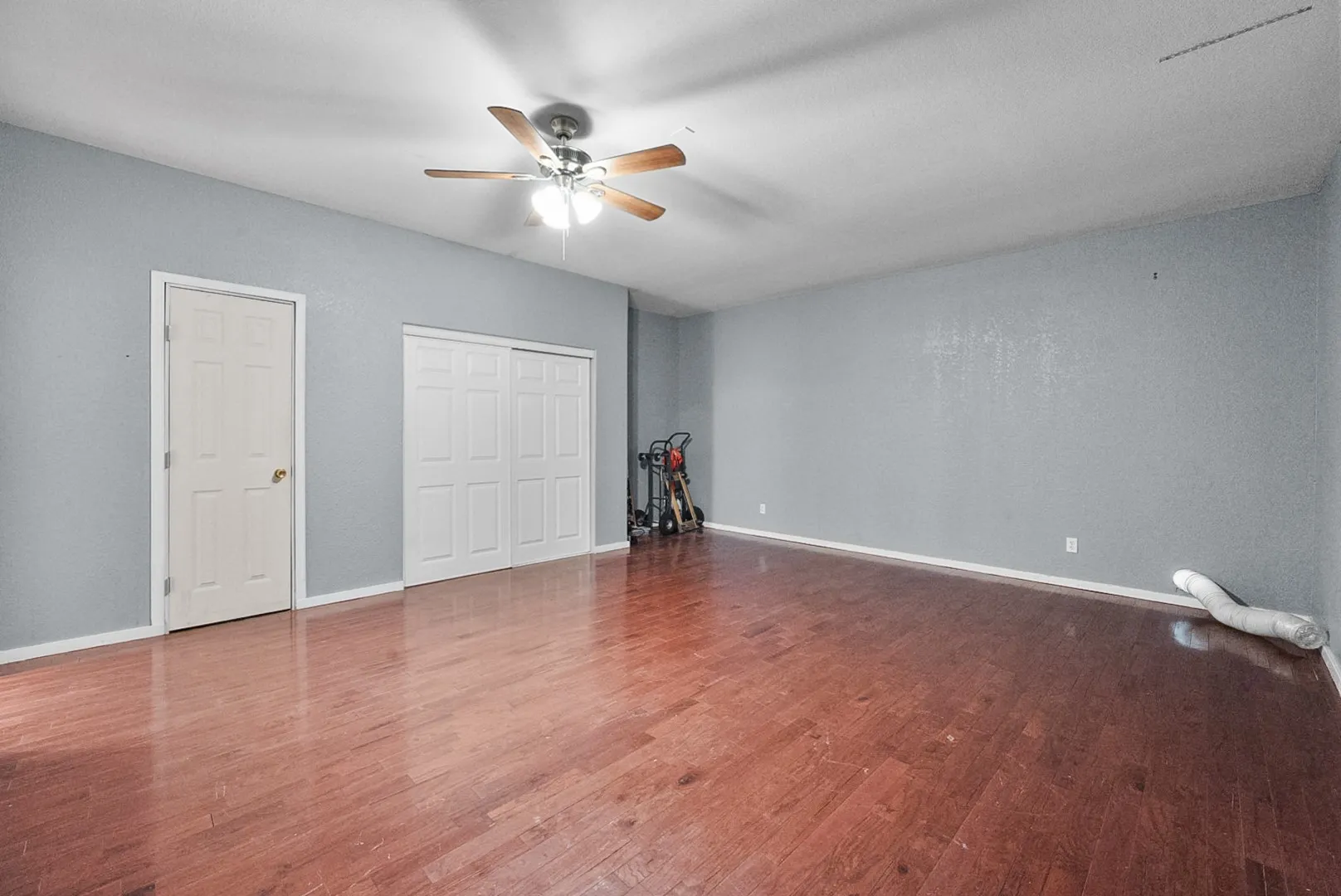 Wood-finish flooring, ceiling fan with integrated lighting, sliding panel closet doors, and a paneled interior door