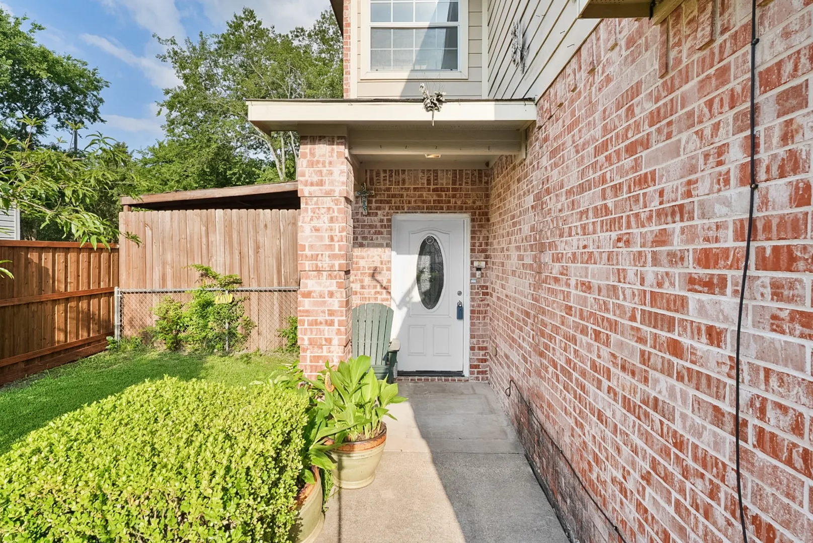 Brick exterior with a covered entry, white paneled door with an oval glass insert, and concrete walkway
