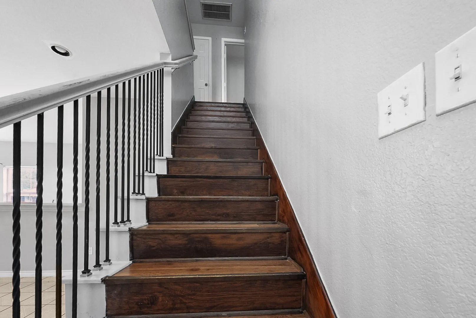Staircase featuring wood-finish treads, a white handrail, and black wrought iron balusters
