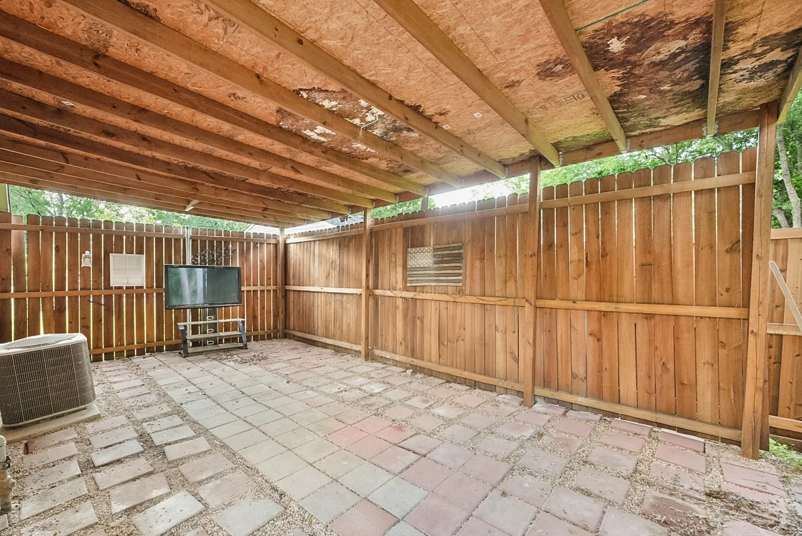 Covered outdoor patio with exposed wood ceiling beams and wood privacy fencing